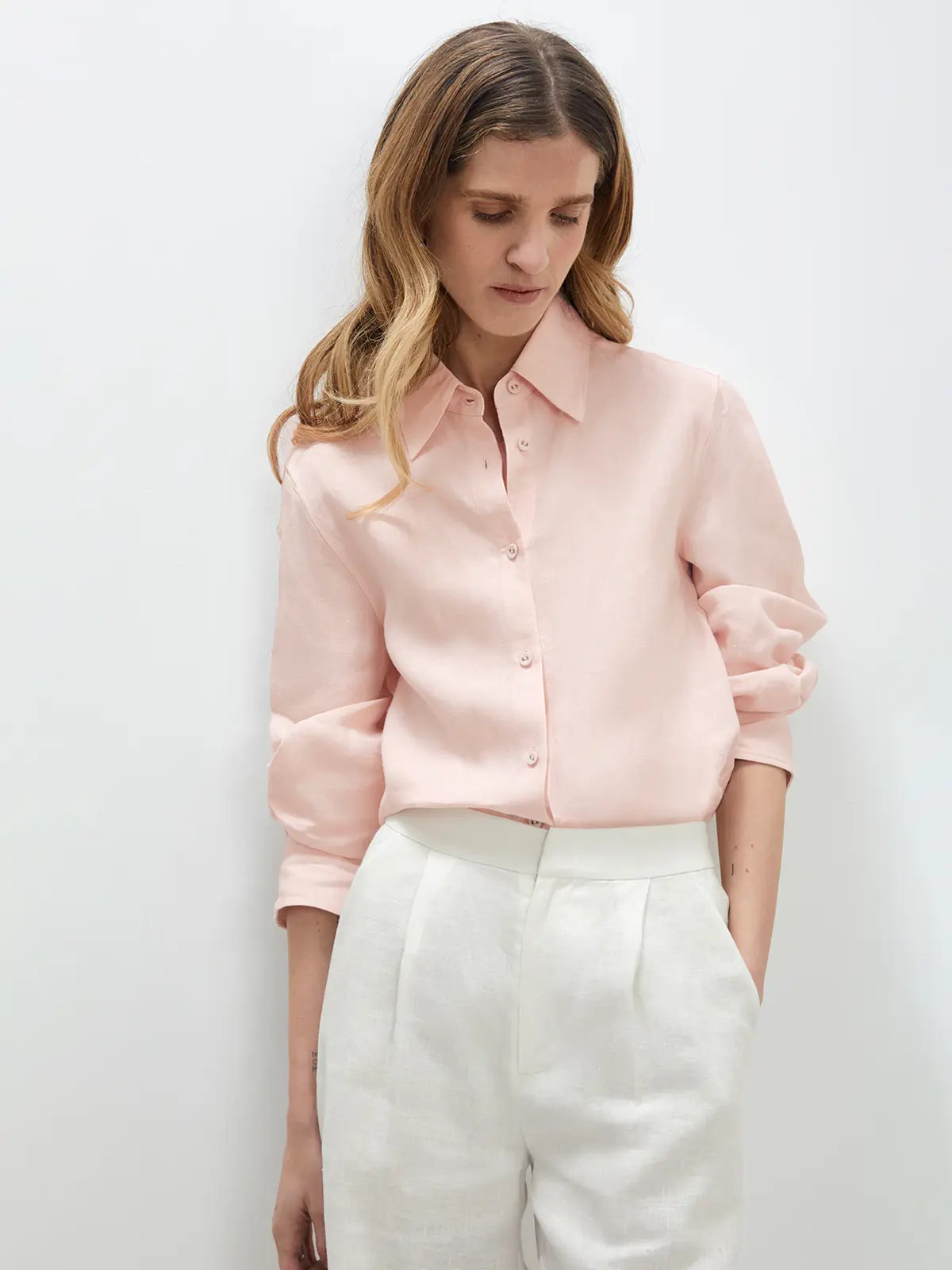 Model standing front-facing in a Pink linen shirt layered under a vest, with light trousers and loafers.