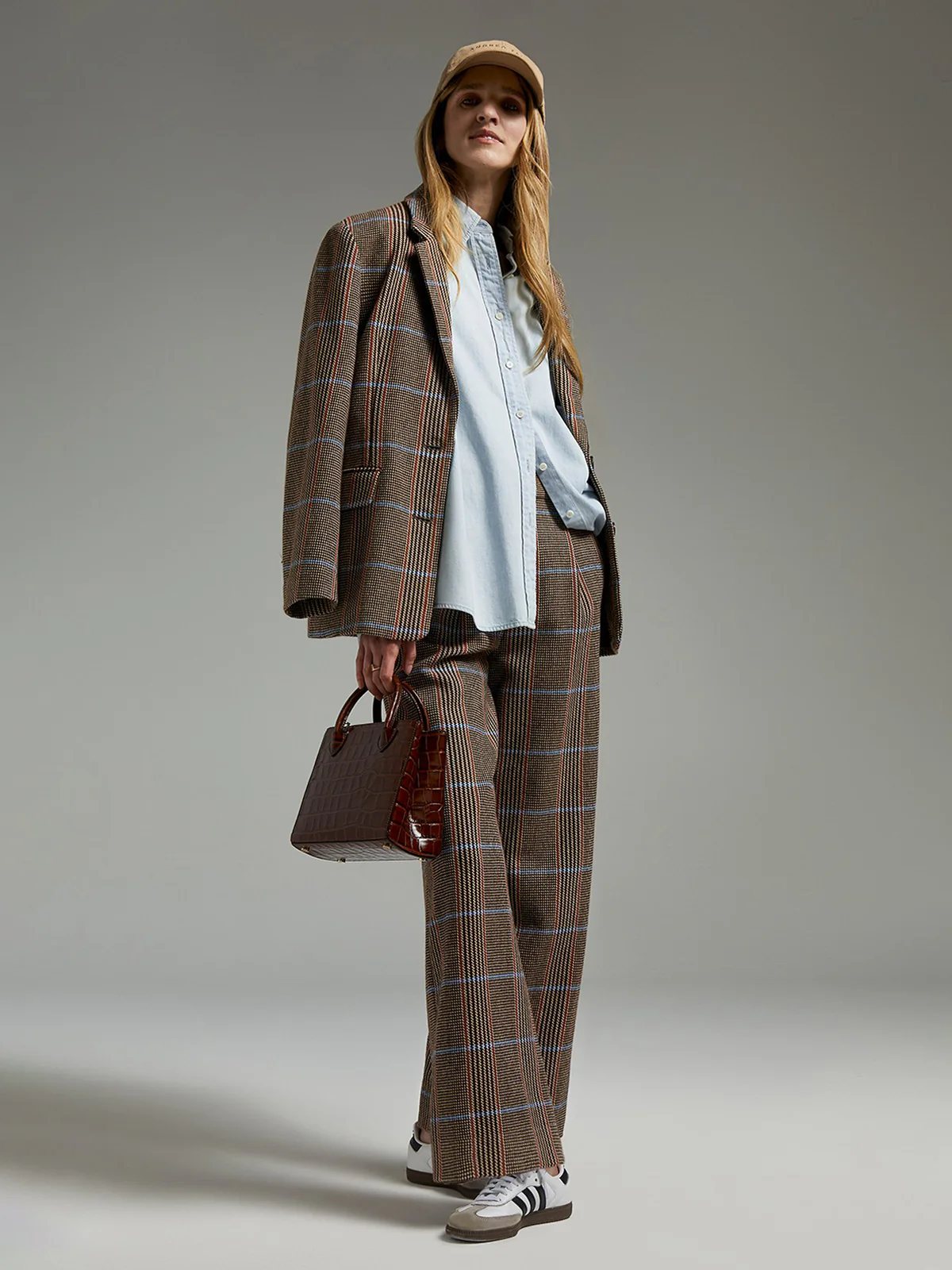 Close-up side view of brown wool British check trousers with pleated front, worn under a matching blazer and top.