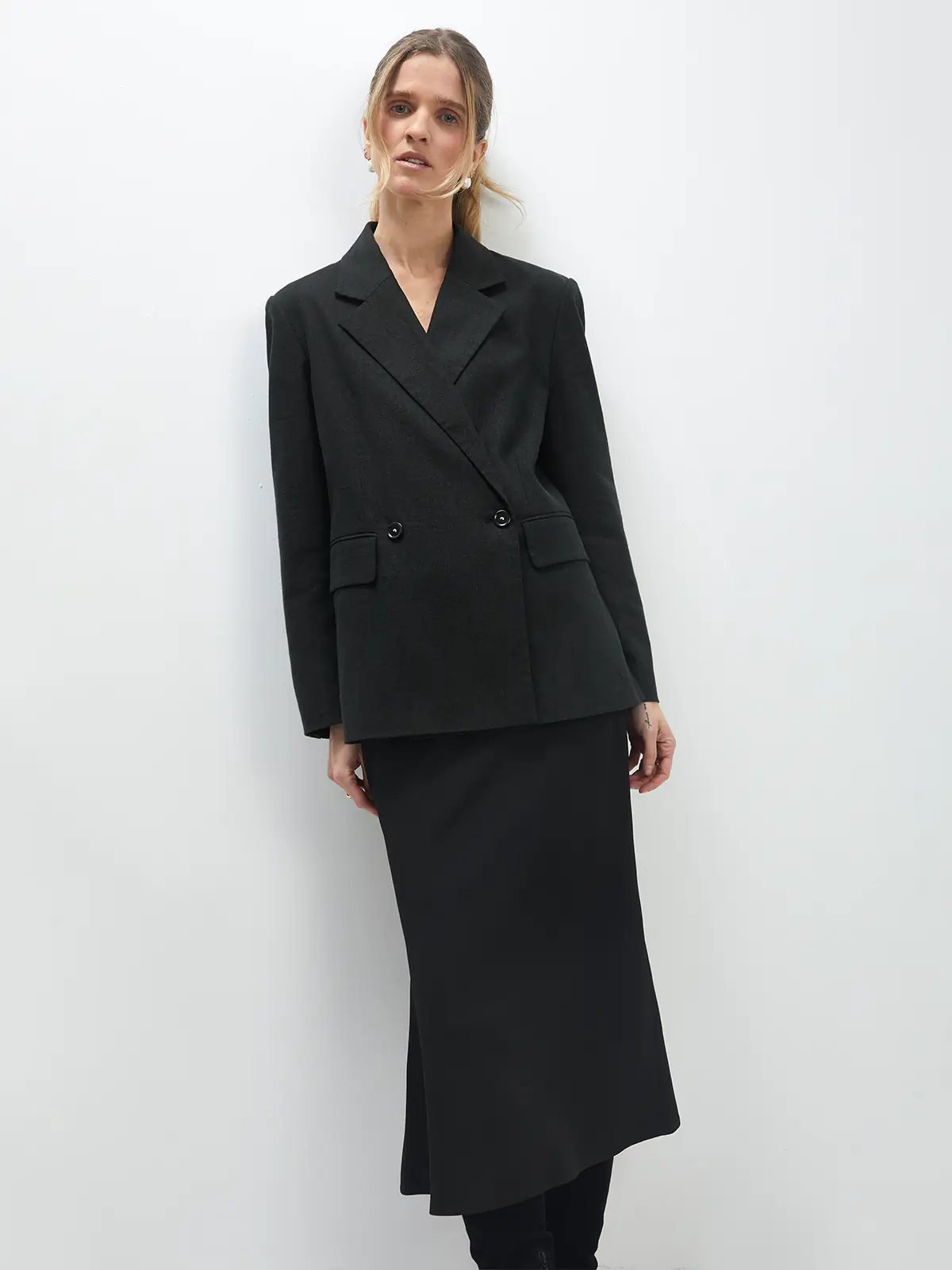 Model in a black acetate mermaid skirt layered under a black double-breasted blazer, front view.