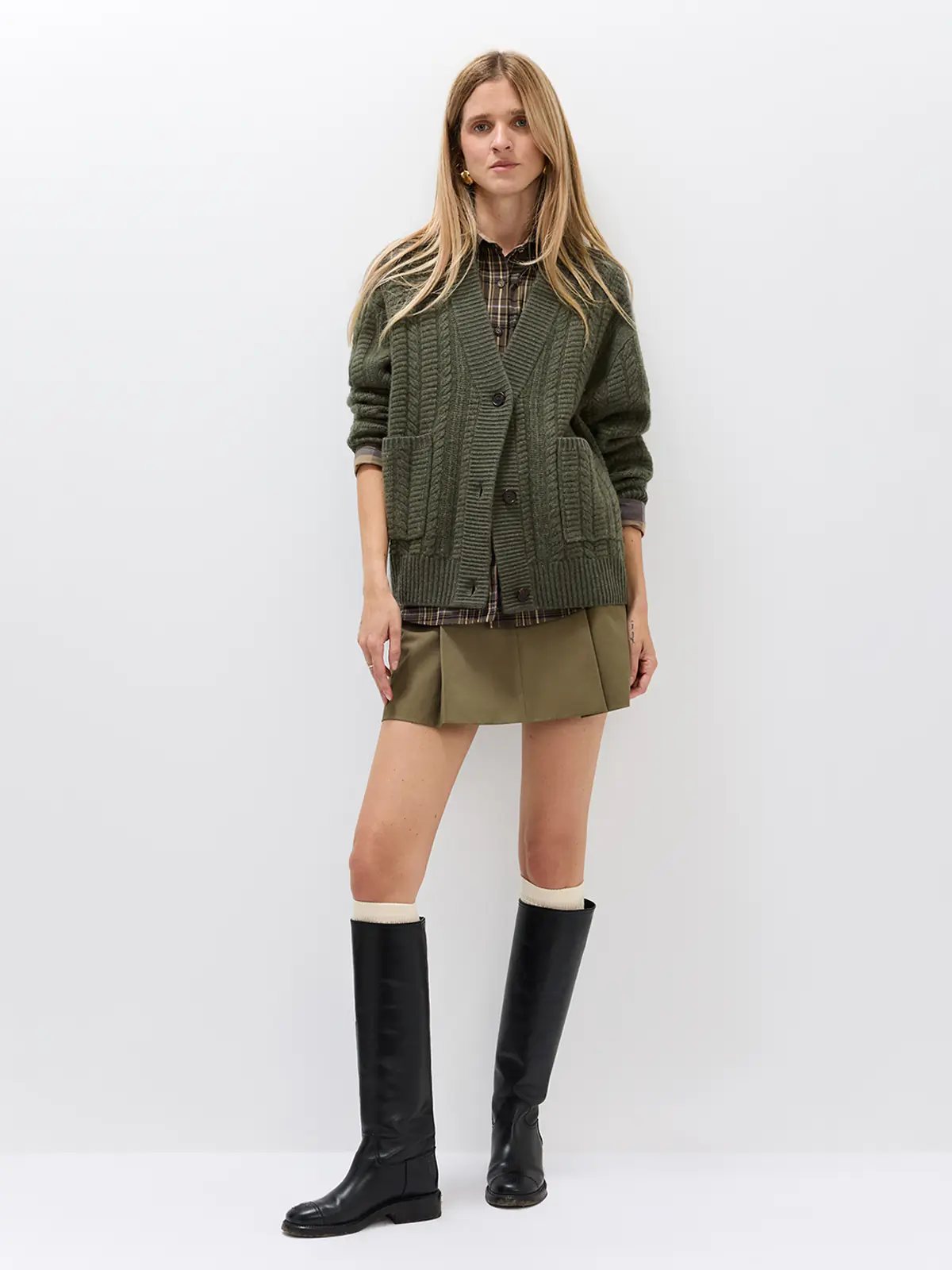 Model wearing a green V-neck cable knit cardigan with front buttons and patch pockets over a matching green knit dress and boots.