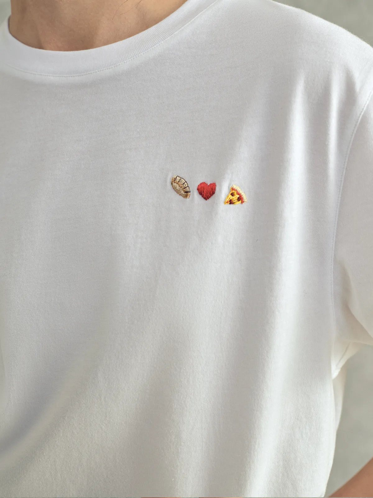 Front chest view of white Lover's T-Shirt showing embroidered bread-heart-pizza design