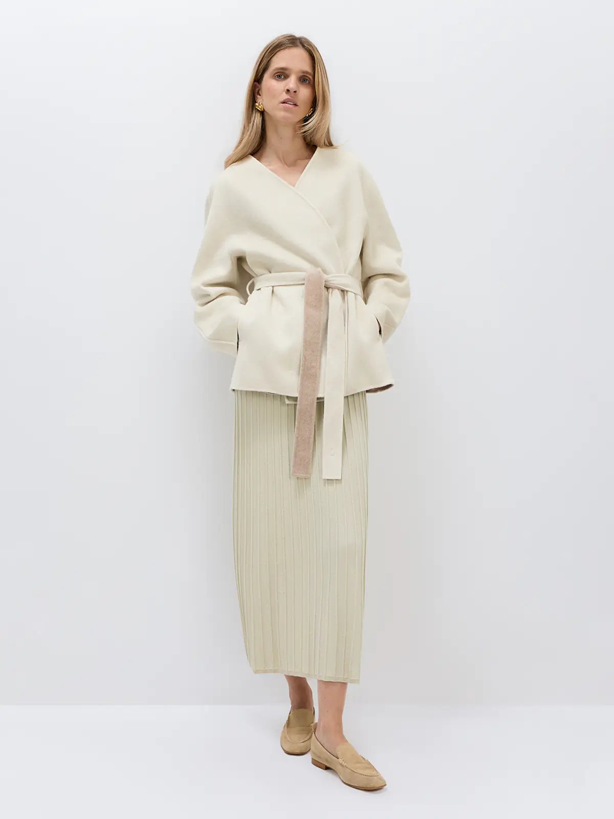 Front view of a model wearing an off-white belted coat with V-neckline, relaxed fit, and tied waist belt.