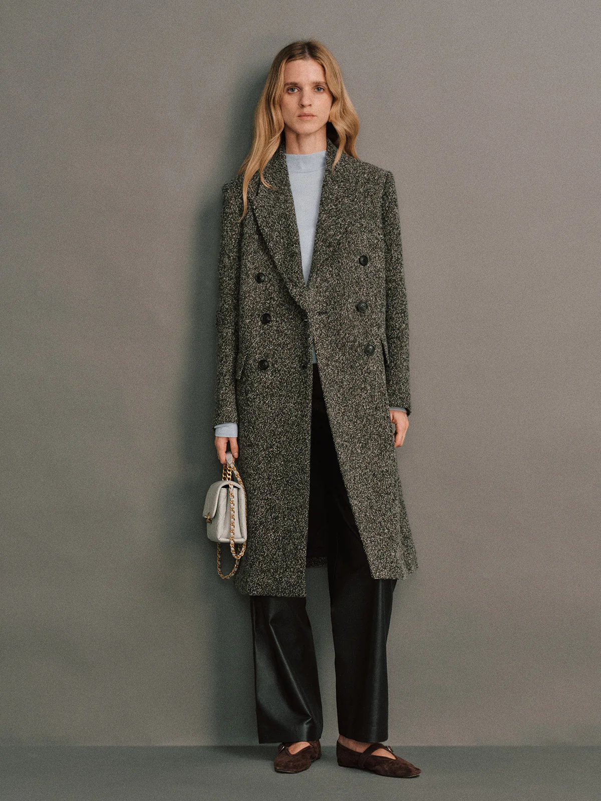 Model wearing a Gray wool bouclé tweed tailored long coat, double-breasted with buttons, over a top and gray skirt.