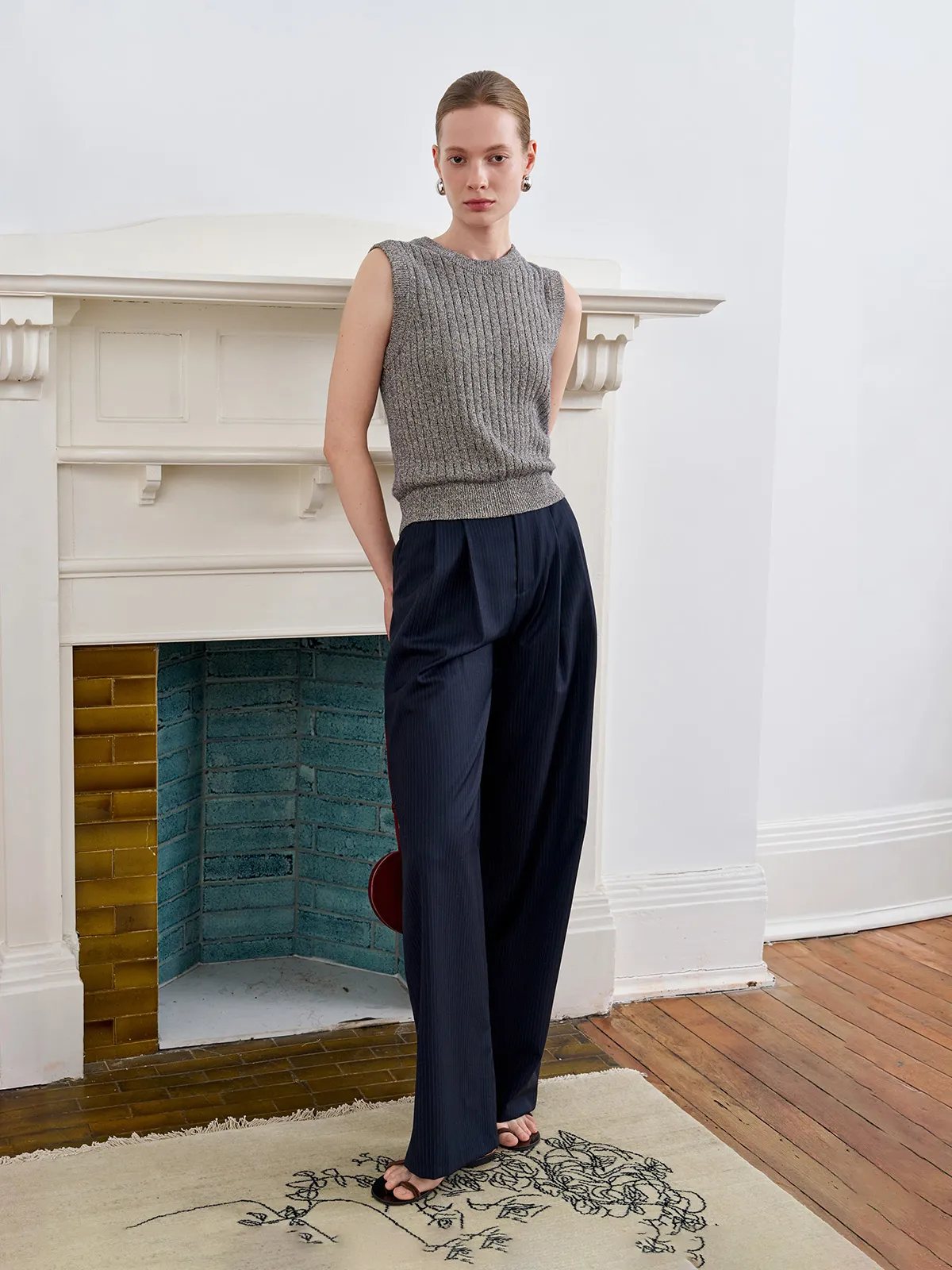 Model in sleeveless ribbed knit top and ROGAN wide leg trousers, standing on embroidered rug