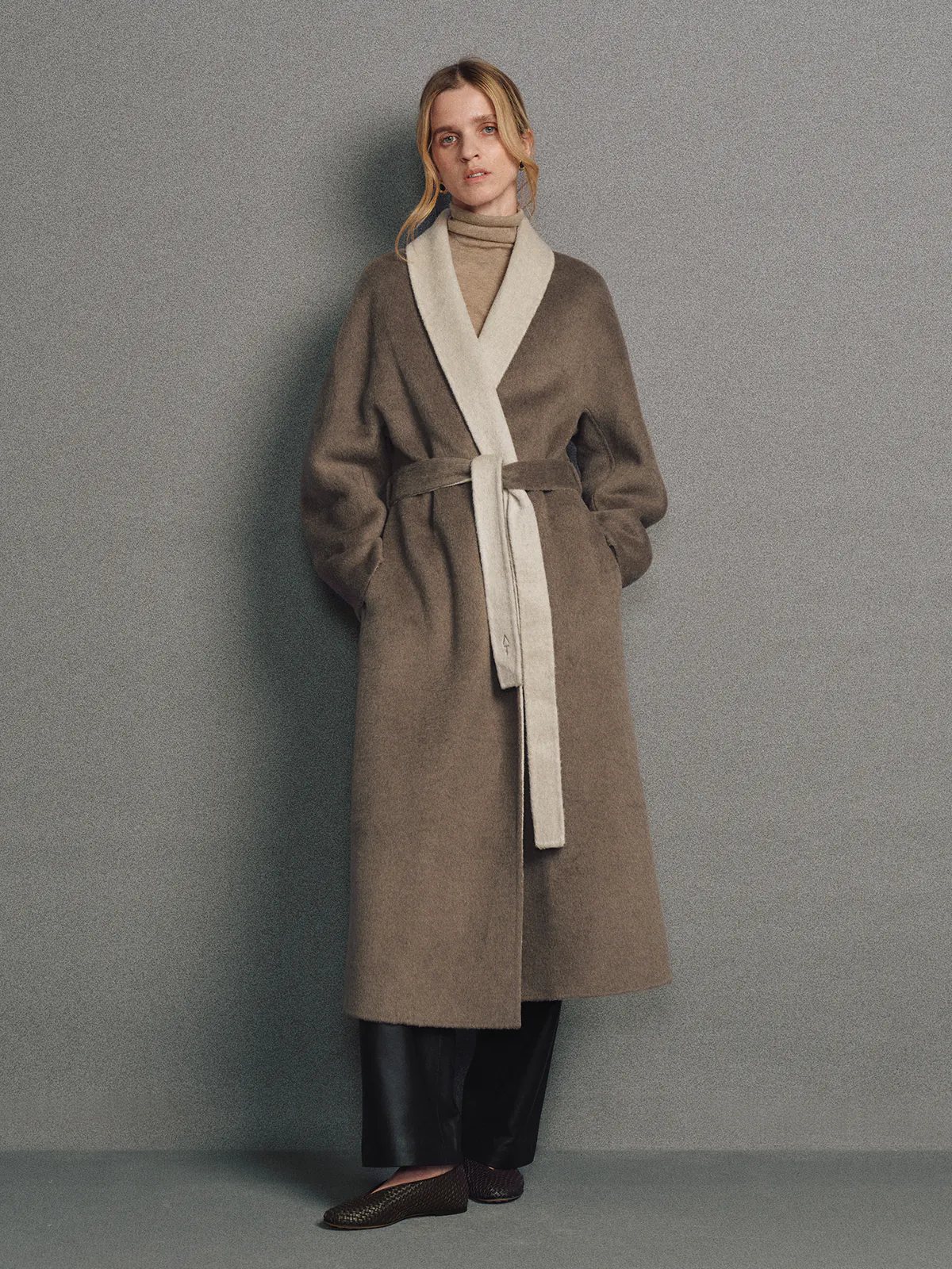Model wearing a brown two-tone reversible notched-collar coat with lapel and belt, hands in pockets.