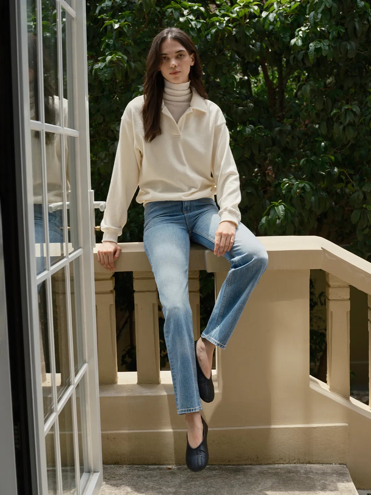 Model sitting on balcony railing wearing JOSETTE jeans with cream polo sweater and turtleneck
