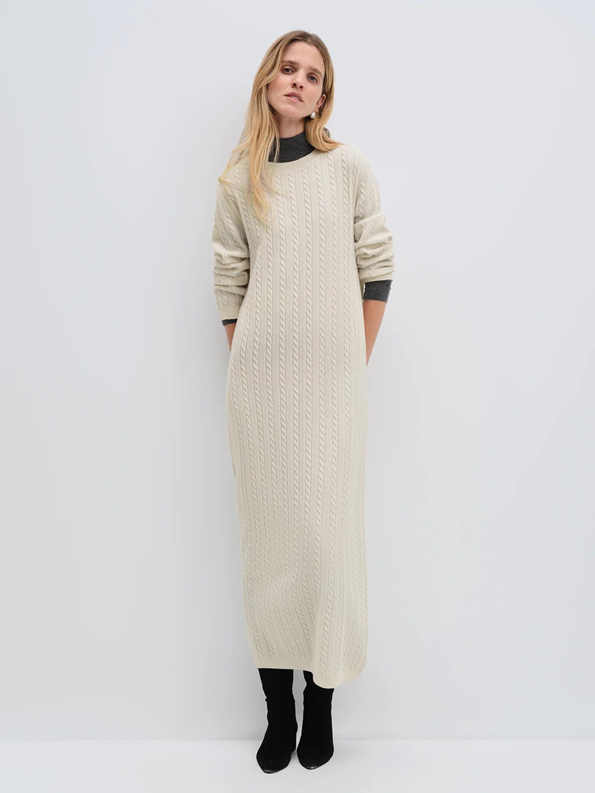 Model wearing andreatang cream Merino wool cable-knit maxi dress with raglan sleeves, styled with tan loafers and clutch