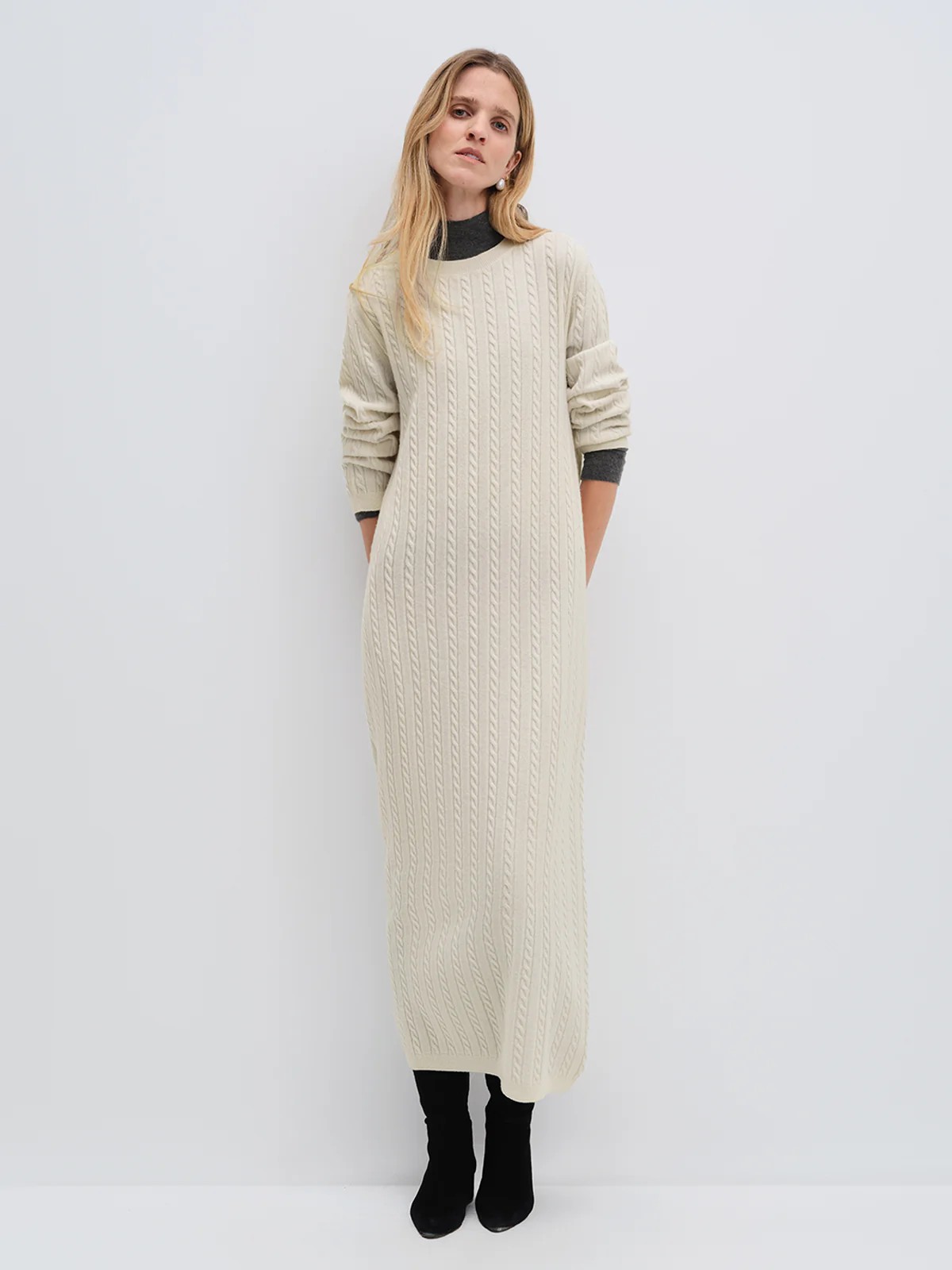 Model wearing andreatang cream Merino wool cable-knit maxi dress with raglan sleeves, styled with tan loafers and clutch