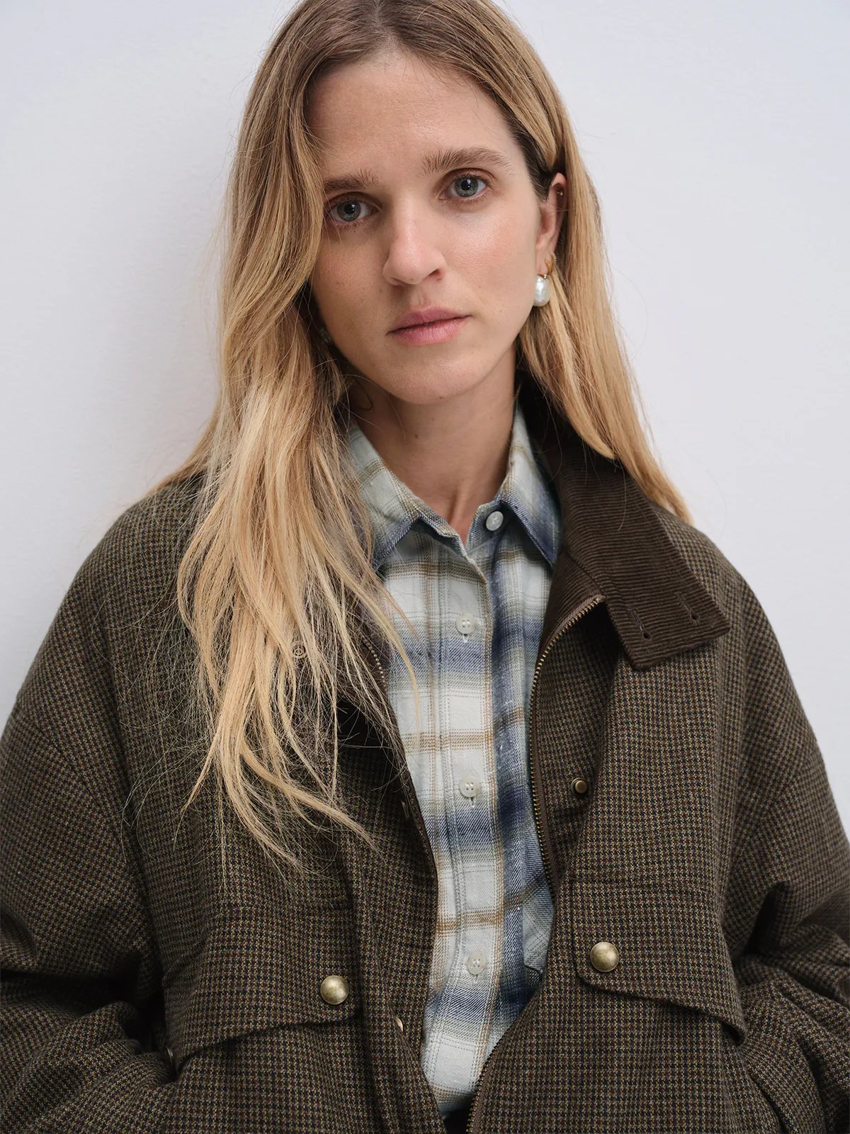 Side pose of model in the Brown houndstooth corduroy reversible jacket over a shirt, holding a brown bag.