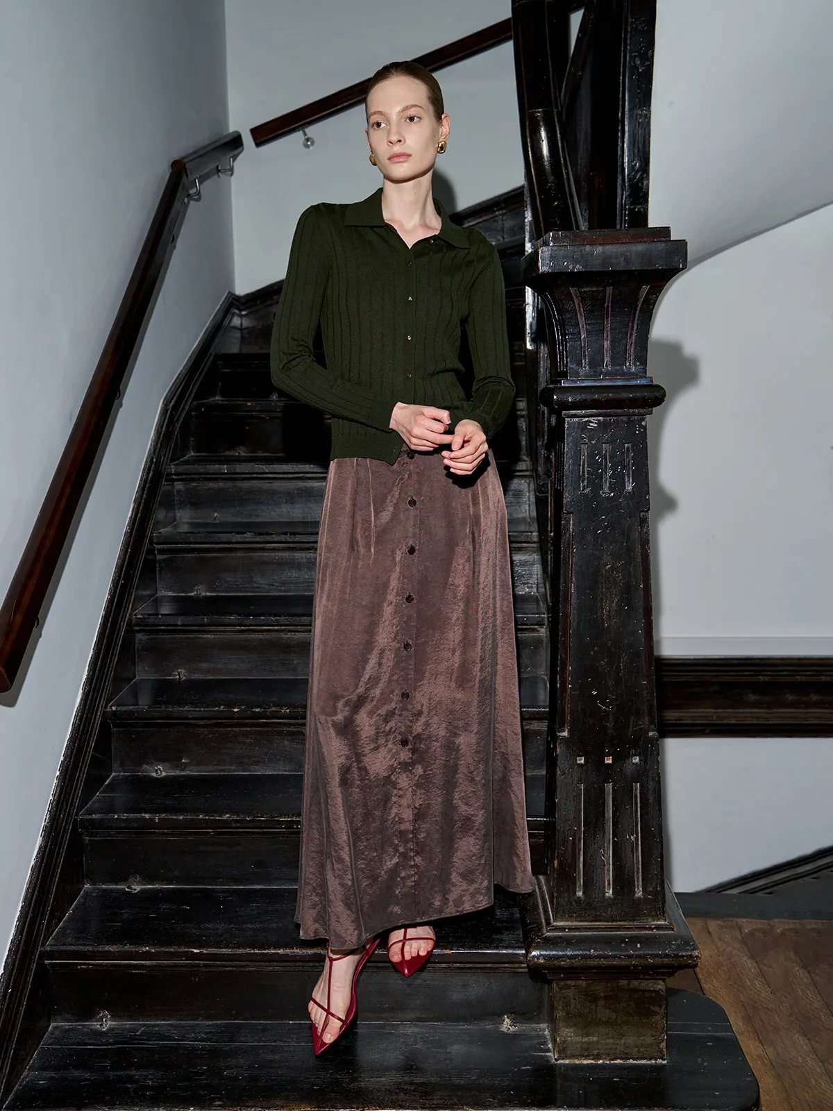 Model in forest green cardigan with brown satin maxi skirt on staircase