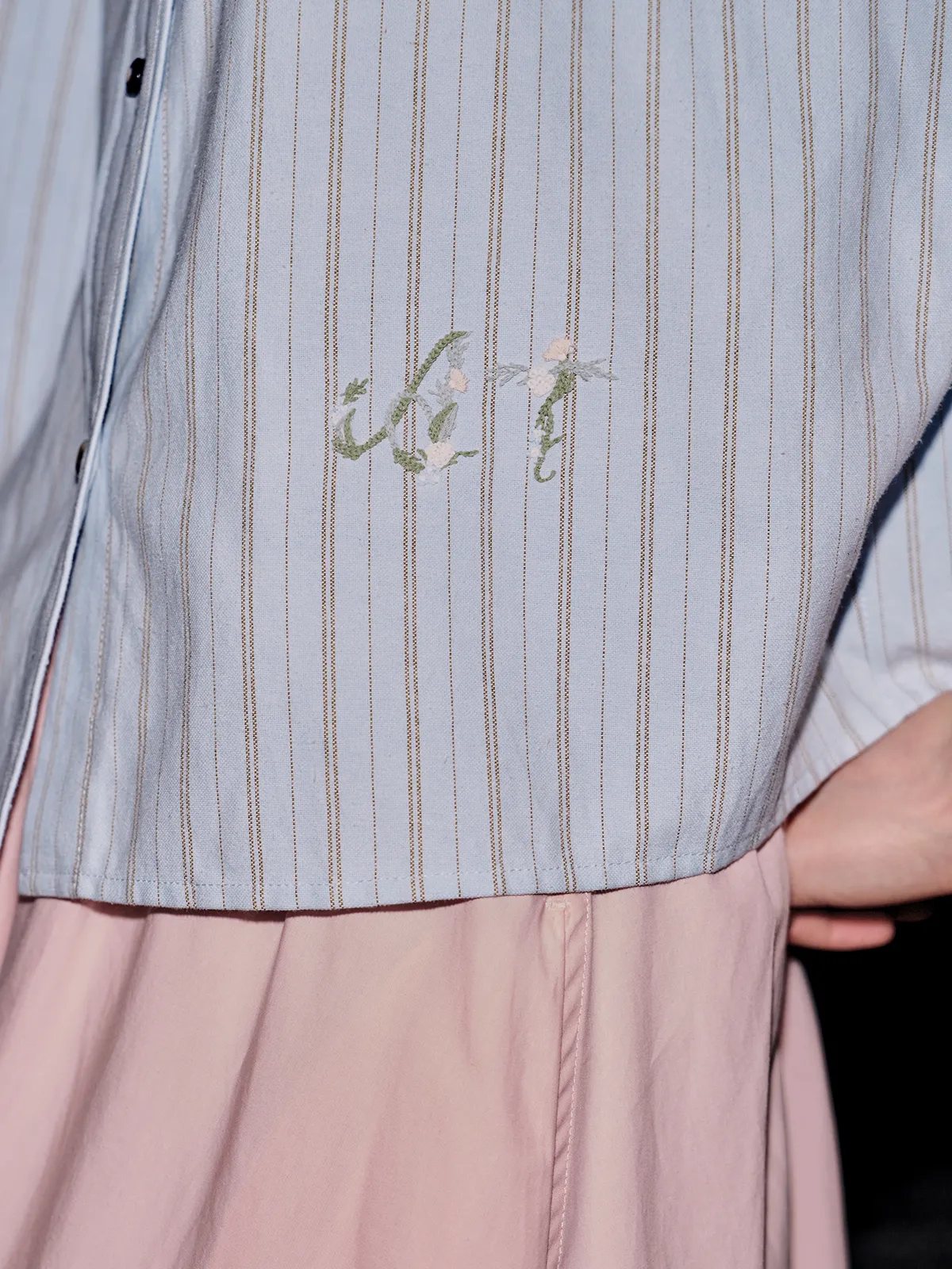 Close-up of floral embroidery on left chest: delicate sage leaves and blush blossoms on striped background