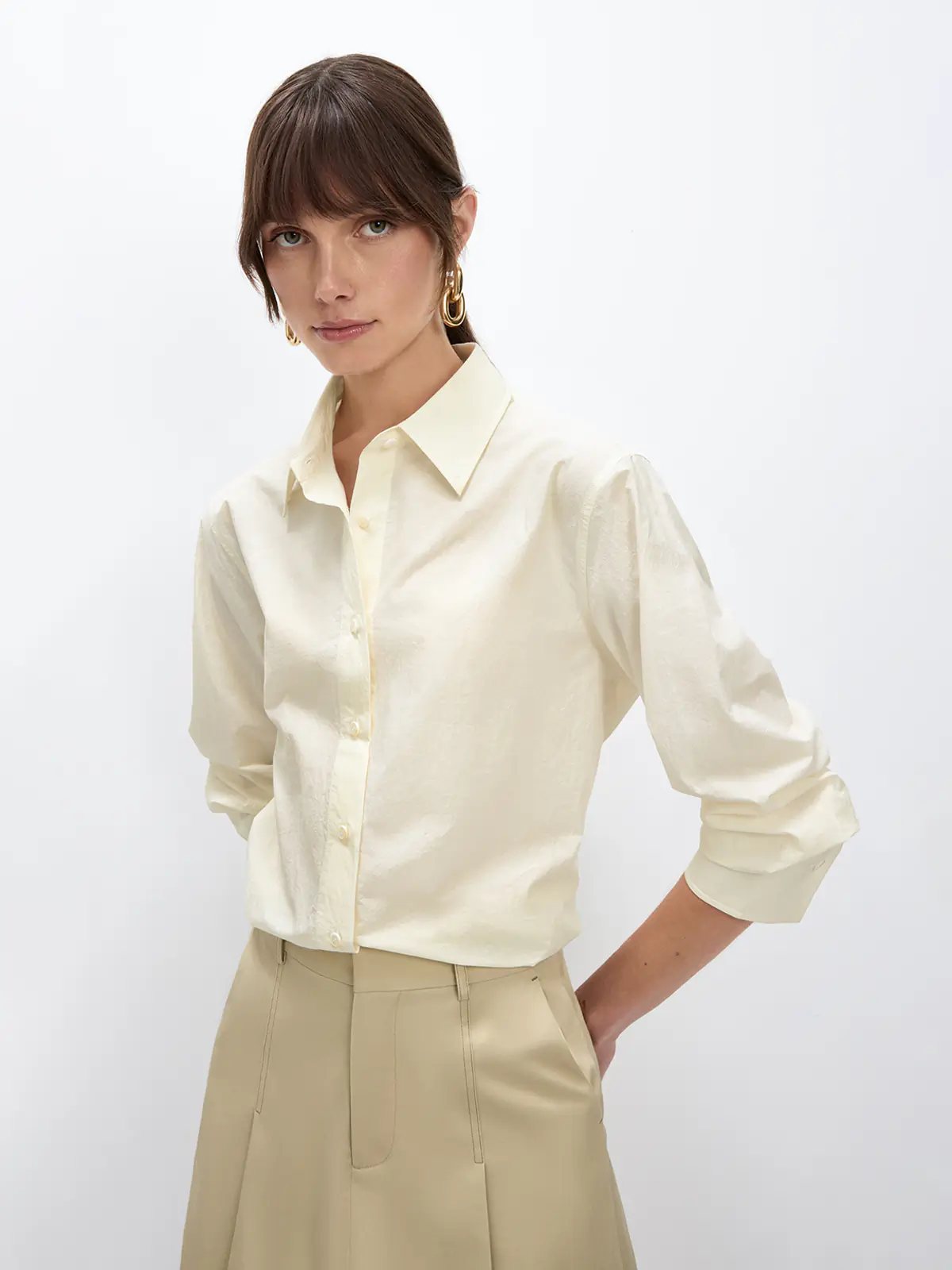Model wearing the Beige NAOMI shirt with rolled sleeves and a pleated skirt, hand on hip.