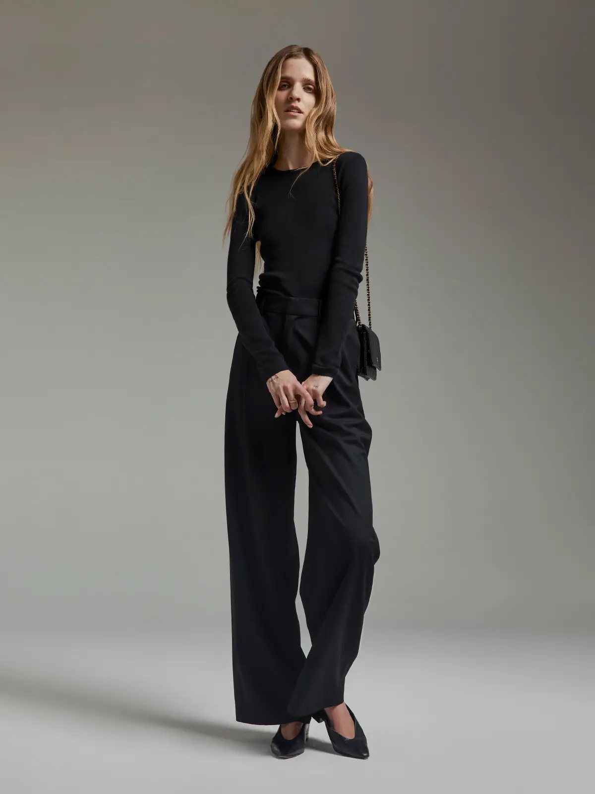 Model in a black slim fit long-sleeve knit top with crew neck and black wide-leg trousers.