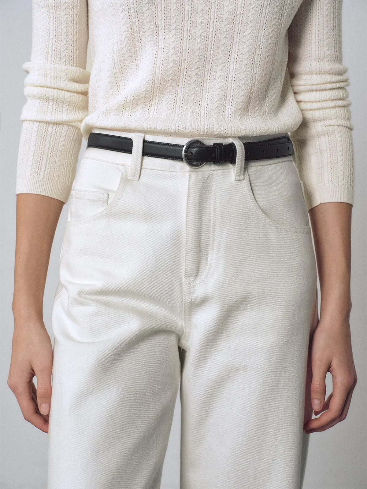Woman wearing black KAY belt with silver buckle, styled with cream wide-leg trousers and knit top
