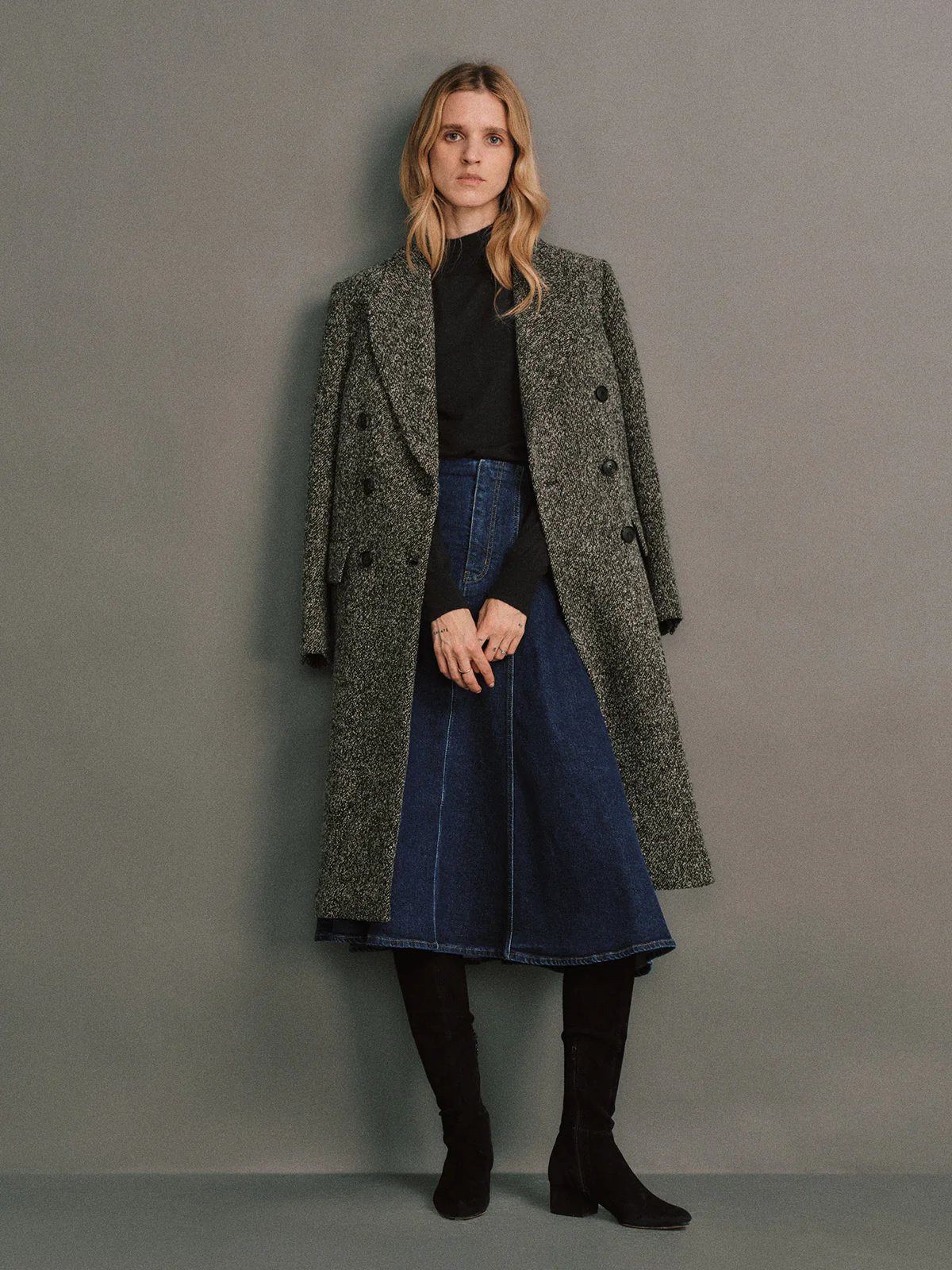 Model wearing a Gray wool bouclé tweed tailored long coat, double-breasted, arms crossed, over a light top with visible cuffs.