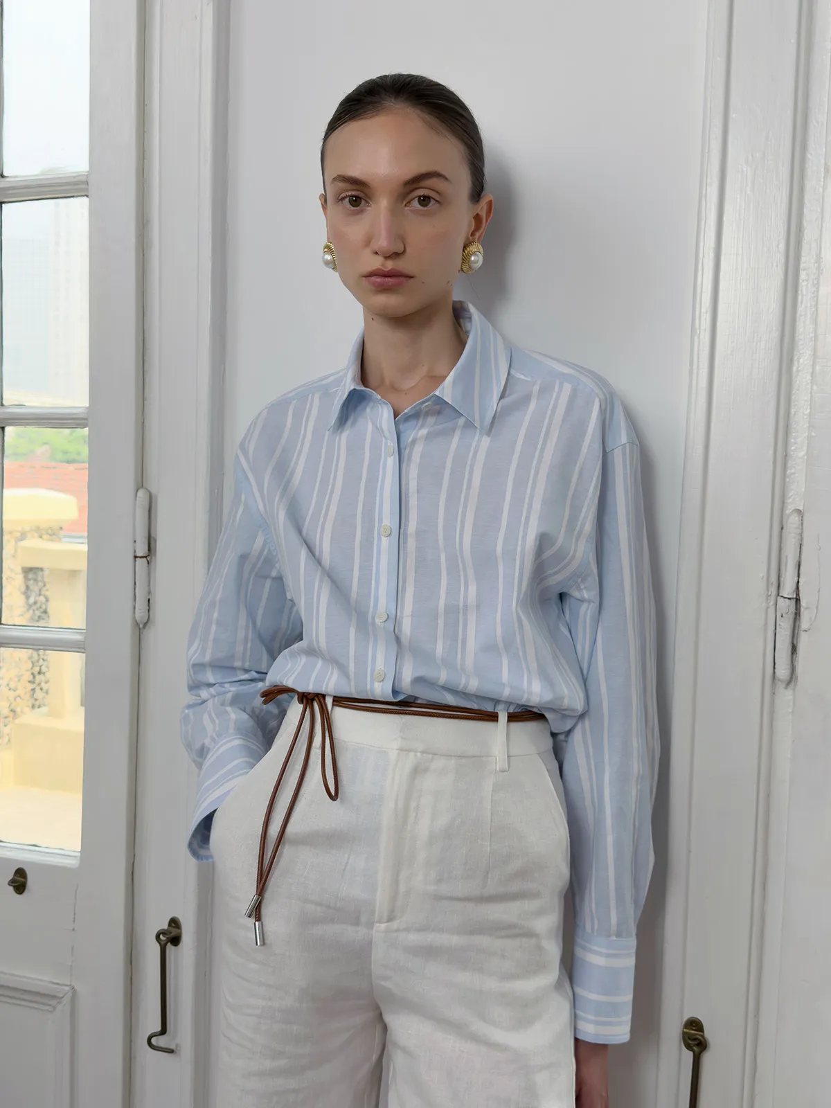 Model wearing blue stripe shirt with white linen trousers and brown leather tie belt