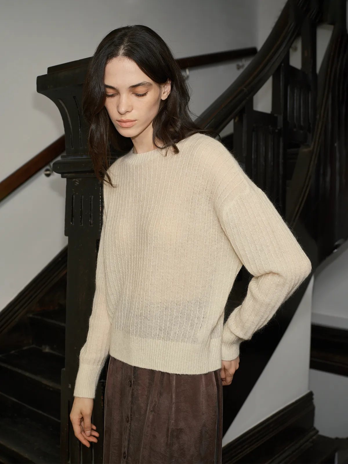 Dark-haired model in ivory ELFIE jumper and brown skirt on black staircase, side profile