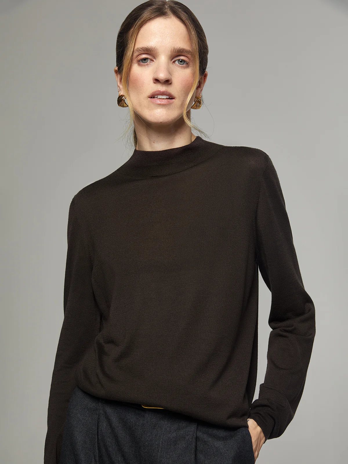 Front view of a model wearing a brown silk lyocell mock-neck top with long sleeves, paired with dark trousers and a brown belt.