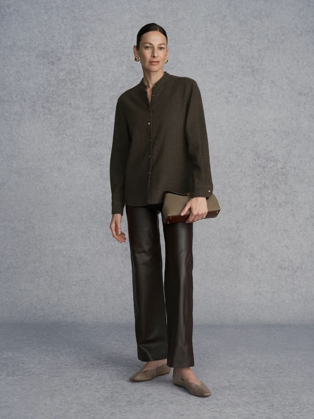 Model wearing WINSLOW wool blend mandarin collar shirt with black leather trousers and clutch, studio portrait