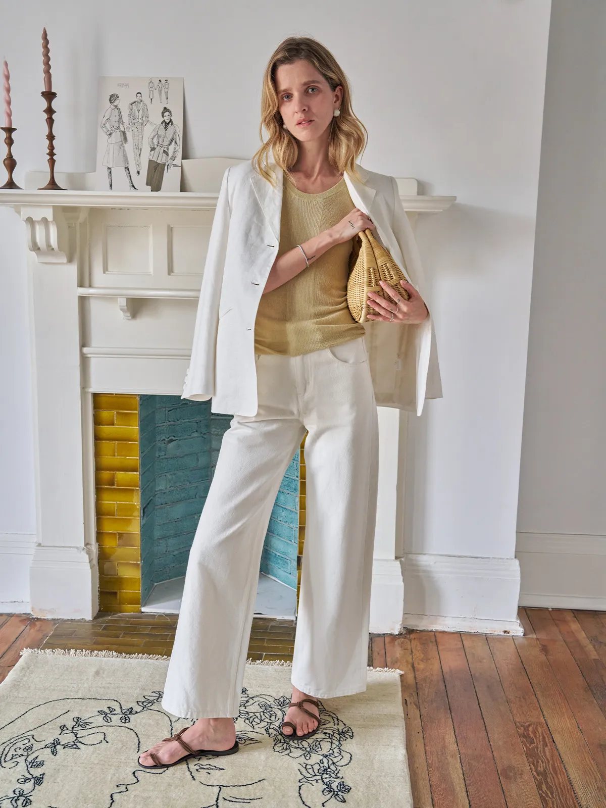 Model in oat MEADOW Textured Knit Tank Top layered under white linen blazer with white wide-leg pants and woven bag, fireplace backdrop
