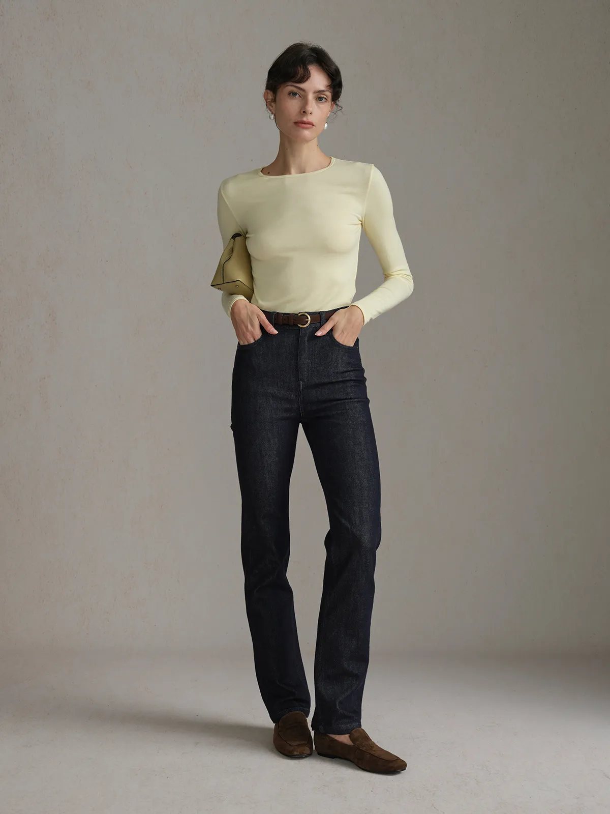Woman wearing Andreatang TRISTA cream long sleeve t-shirt with dark denim jeans and leather belt, minimalist street style