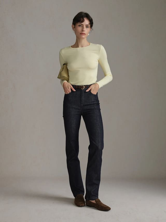 Woman wearing Andreatang TRISTA cream long sleeve t-shirt with dark denim jeans and leather belt, minimalist street style