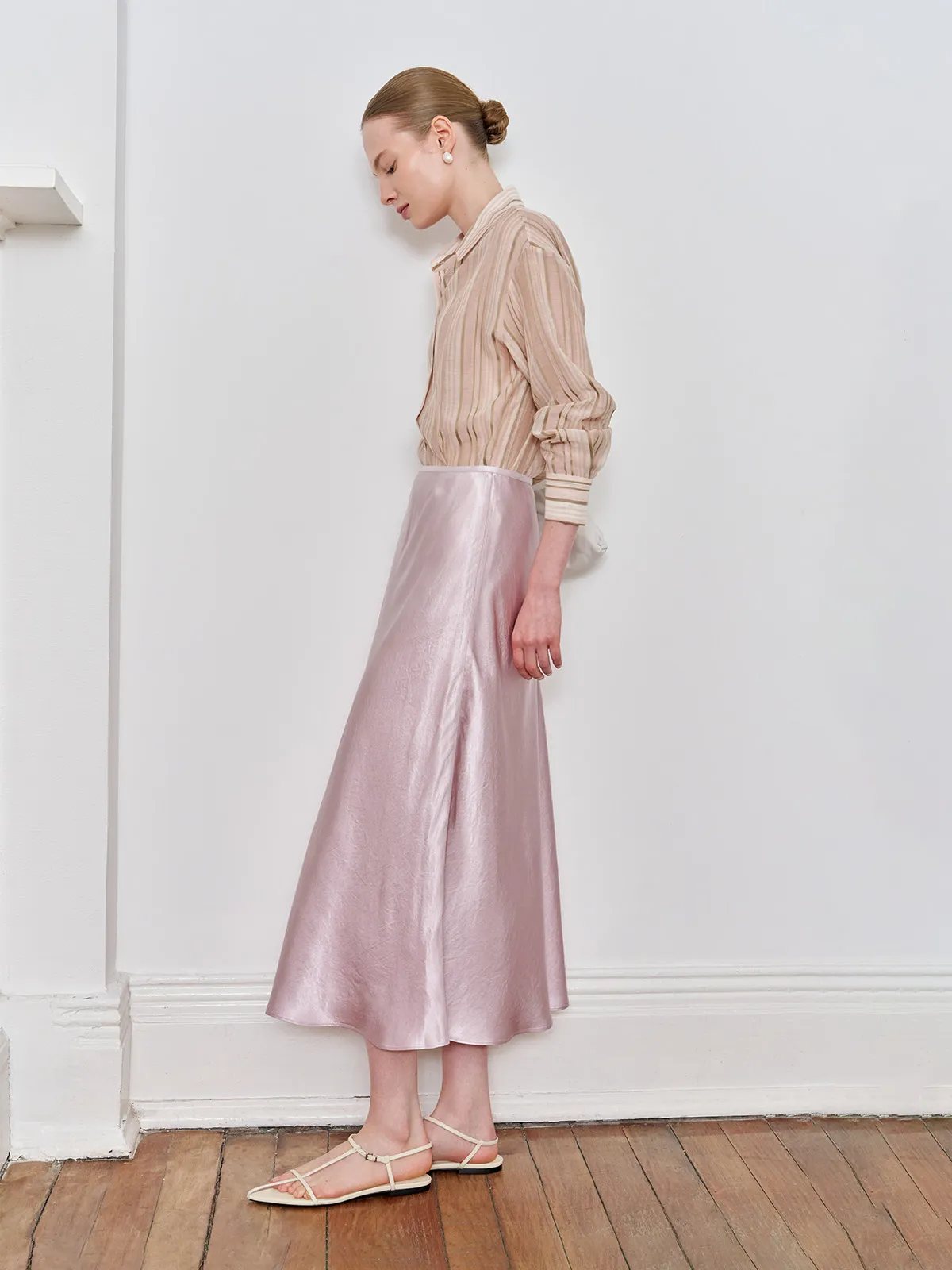 Model in profile wearing SHELL skirt with beige striped shirt, standing against white wall
