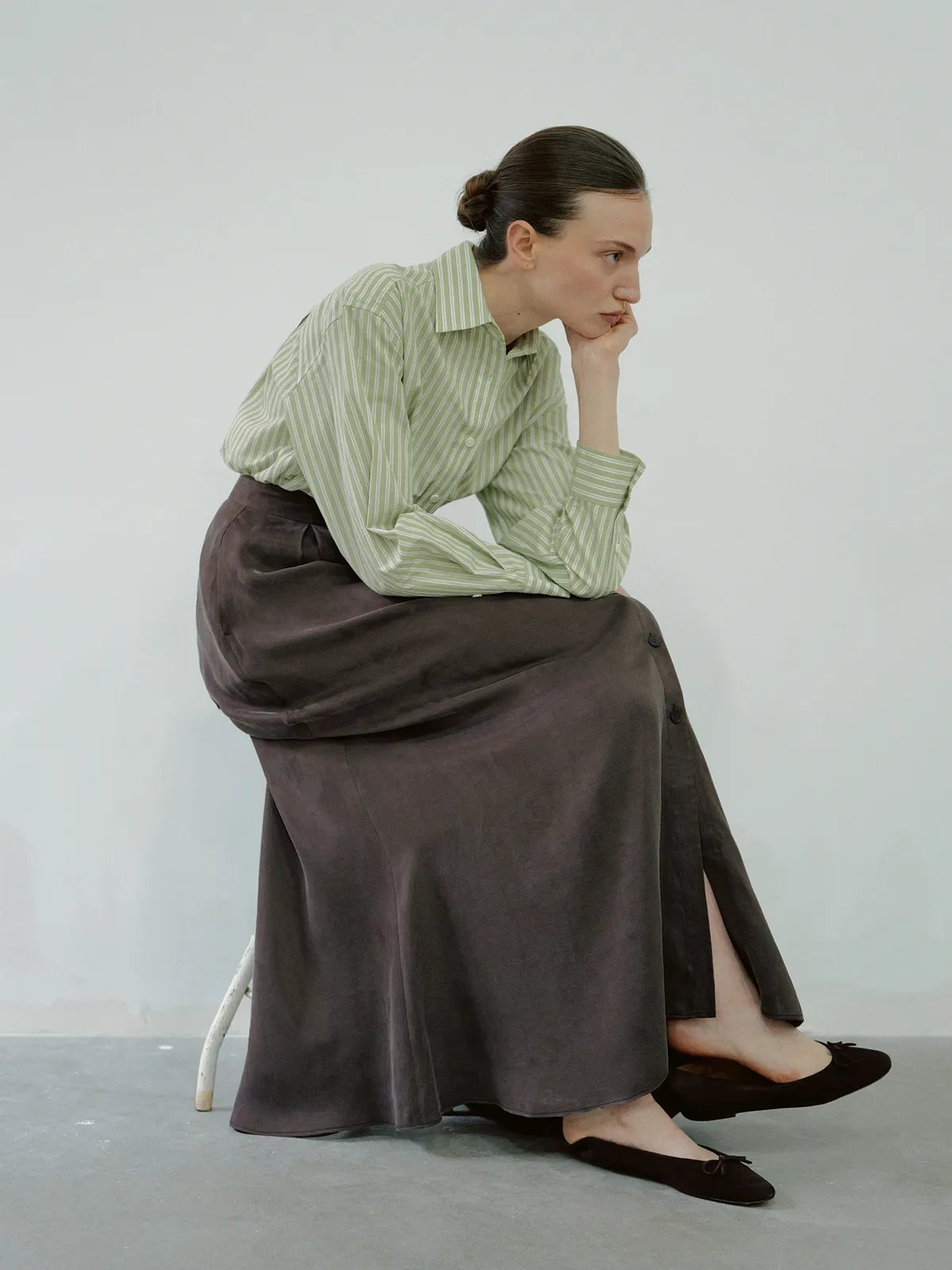 Model seated in taupe NOBU Maxi Skirt with green striped shirt, contemplative pose