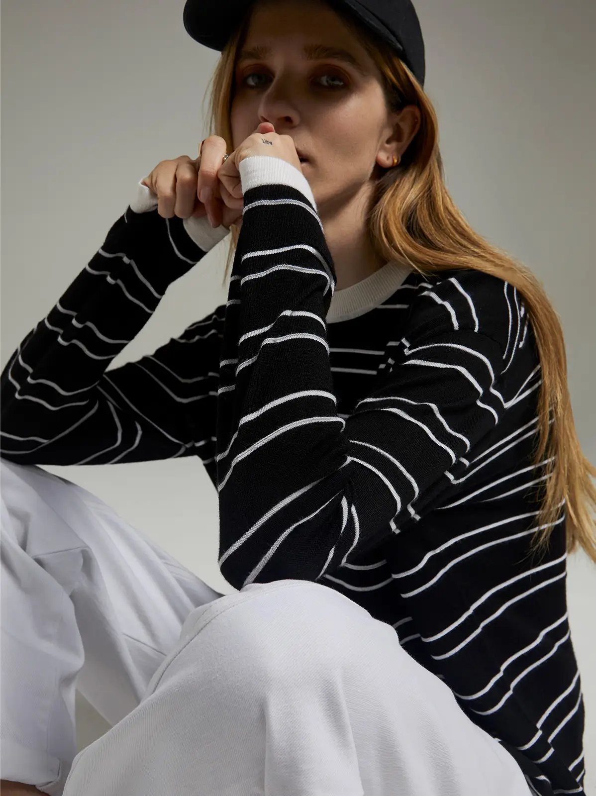 Close-up of model seated, wearing a black knit top with horizontal stripes and pants.