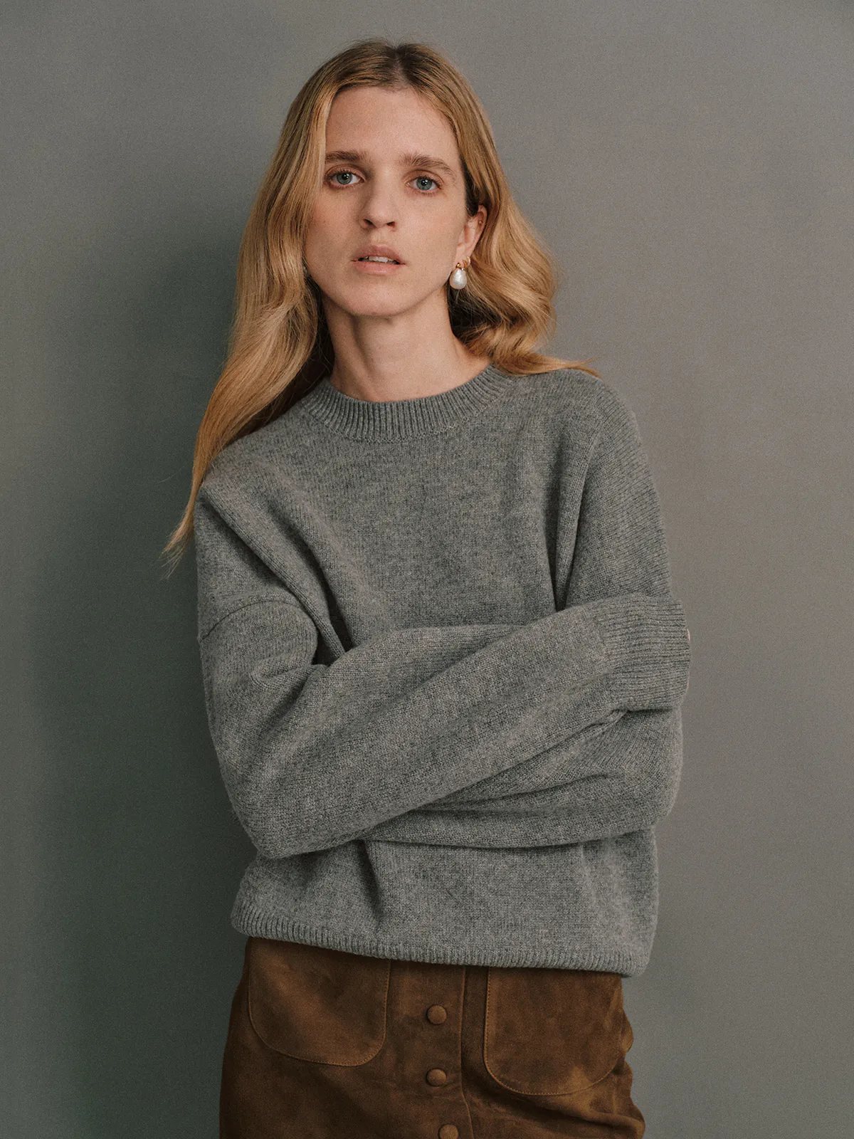 Model wearing a Bottle Green merino wool crewneck jumper with wide-leg trousers and holding a croc-effect bag.