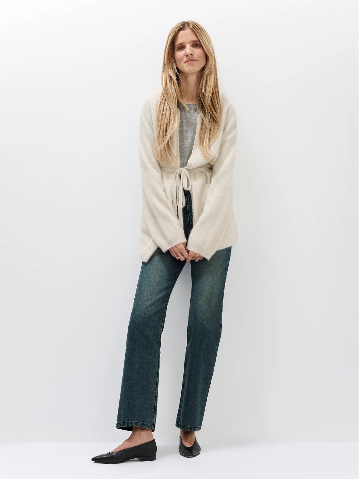 Model wearing the Oatmeal cardigan open over a top and dark jeans, hands clasped at waist.