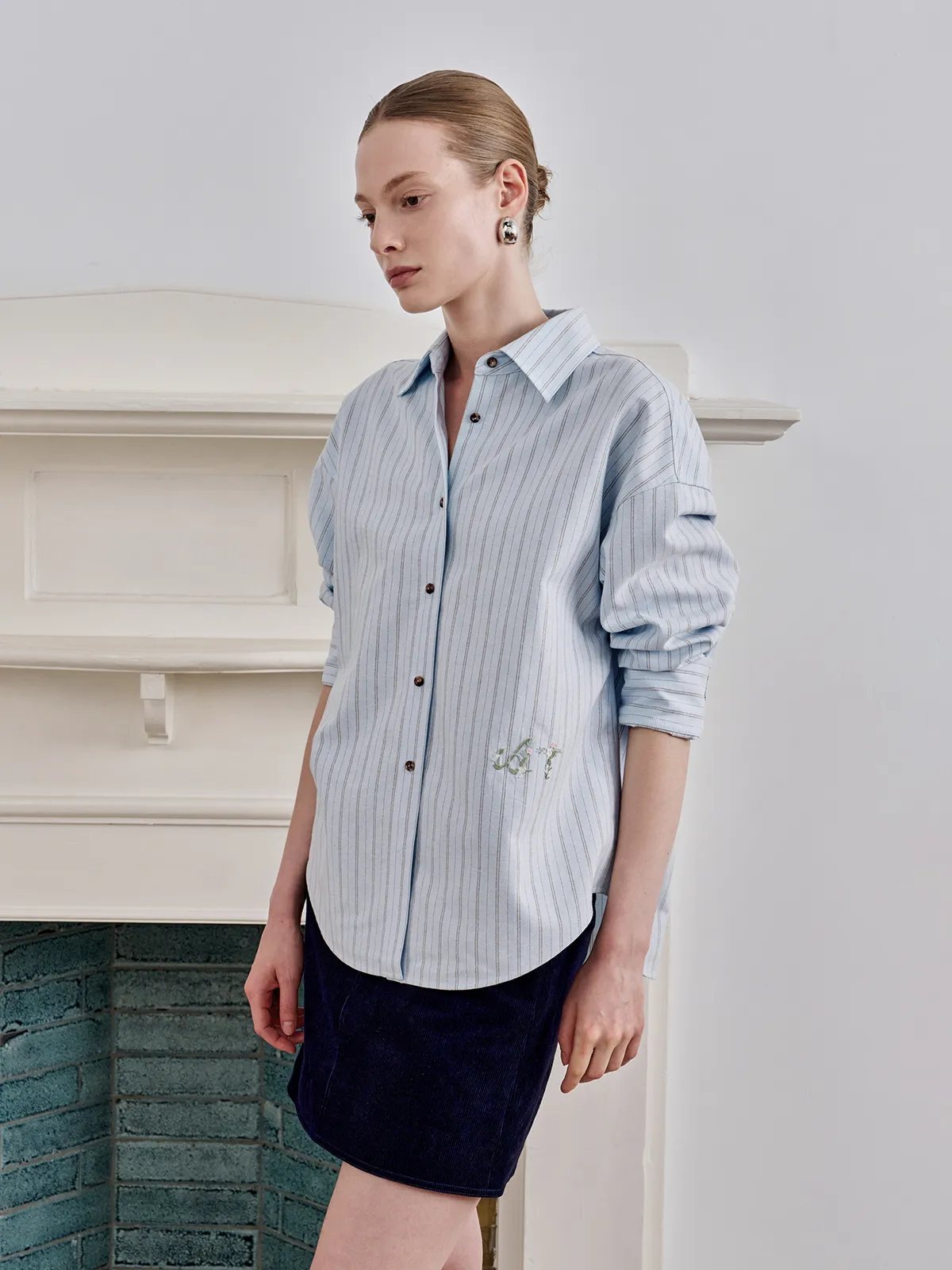 Model wearing TILLY shirt with navy corduroy mini skirt, front view against white fireplace mantel