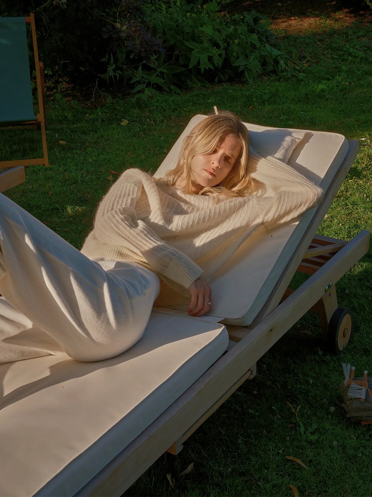 Model reclining on outdoor lounge chair in ivory ELFIE jumper and white trousers, golden hour lighting