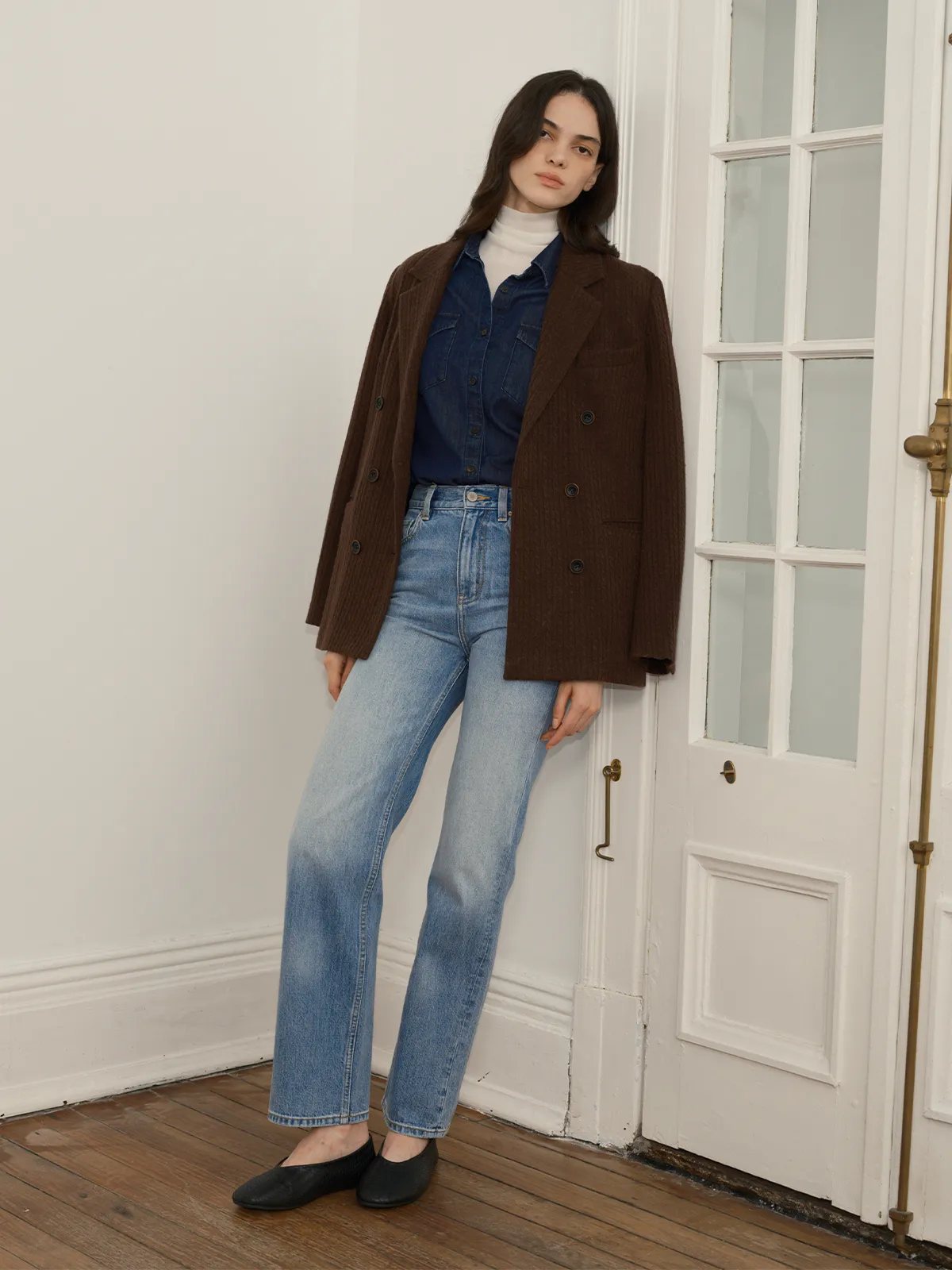 Model leaning against white door wearing JOSETTE jeans with brown corduroy blazer and denim shirt