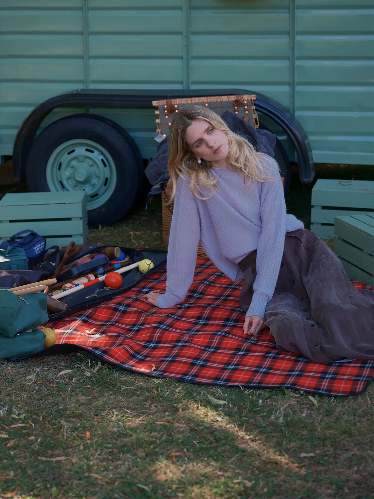 Model seated on red tartan picnic blanket wearing lavender ELFIE jumper, vintage trailer background