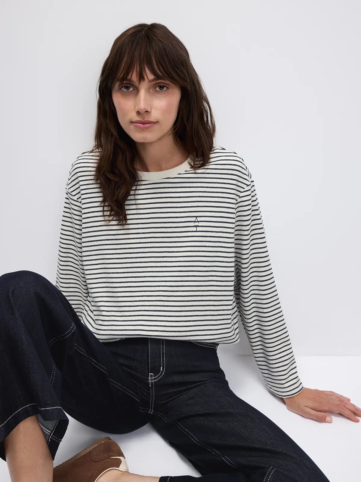 Model seated wearing a Black/White horizontally striped long-sleeve t-shirt with a small logo on the chest.