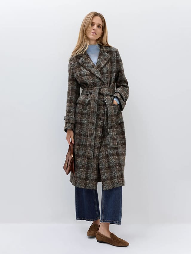 Model wearing a Dark Brown wool alpaca tweed check coat with belt, hands in pockets, over a light top and wide-leg jeans.
