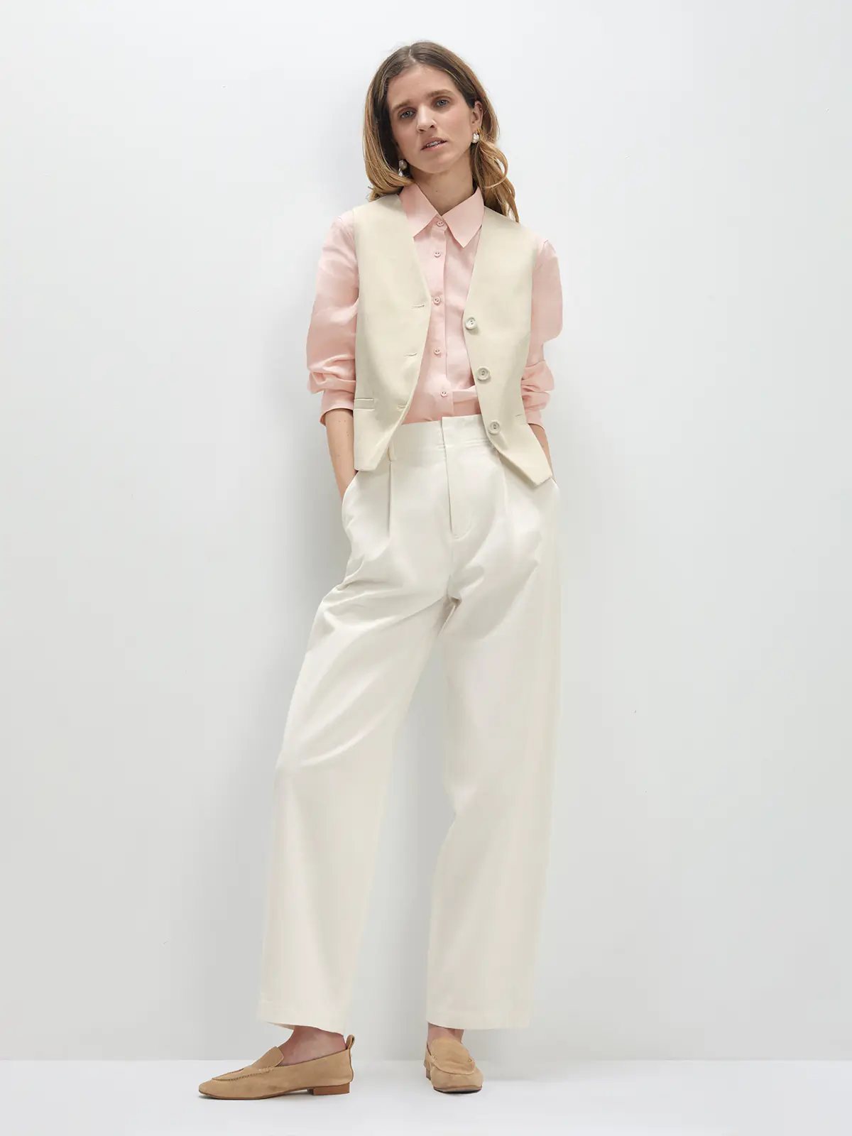 Side profile of model adjusting earring, wearing a Pink linen shirt with relaxed fit and dark trousers.