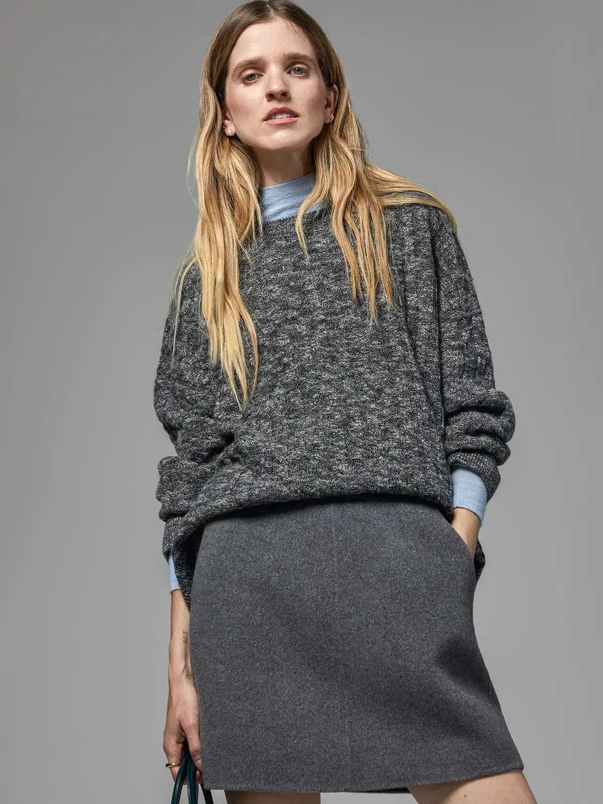 Mixed Gray short A-line skirt worn under a textured gray sweater with rolled sleeves.