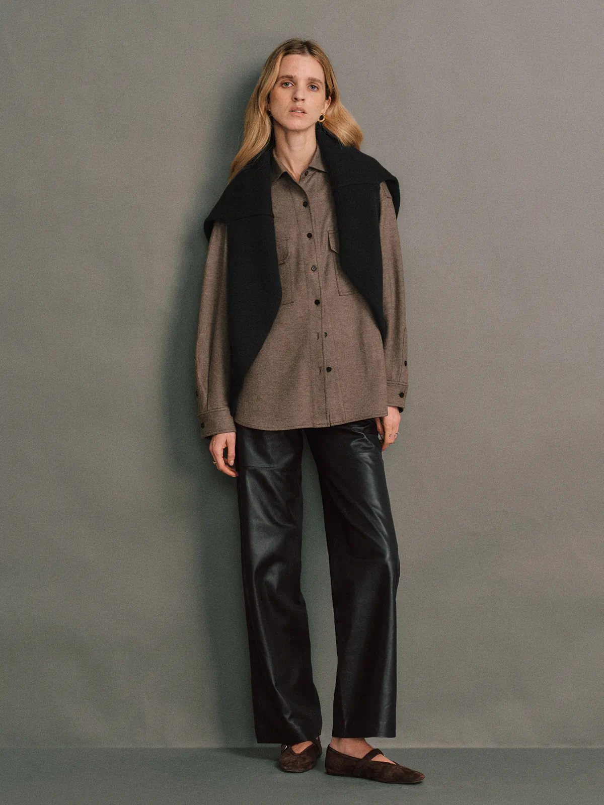 Side view of a model wearing Black soft leather straight trousers layered under a tweed blazer and top.