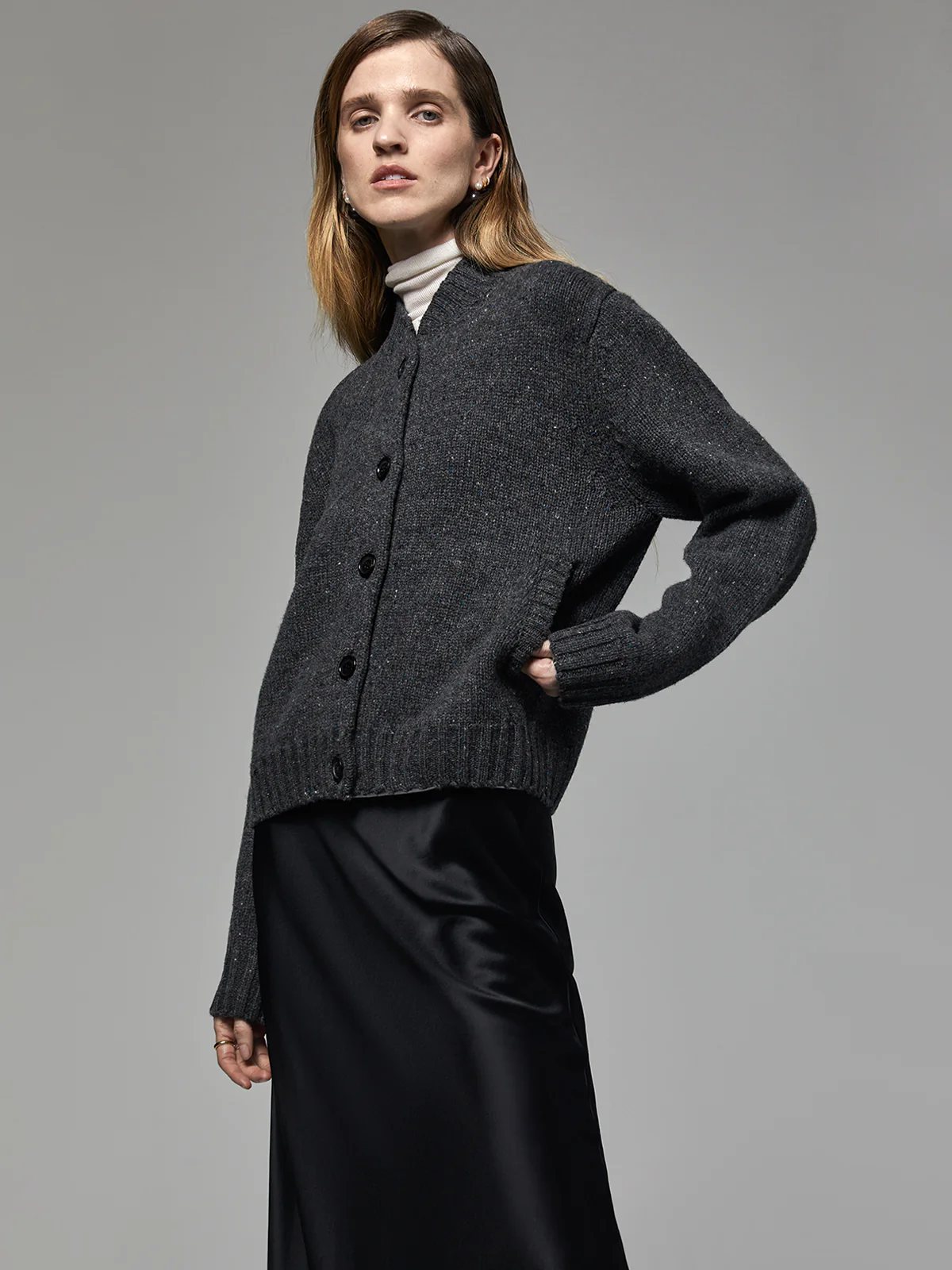 Model in the Dark Gray Merino Wool Baseball Cardigan layered over a turtleneck, paired with a satin skirt and boots.