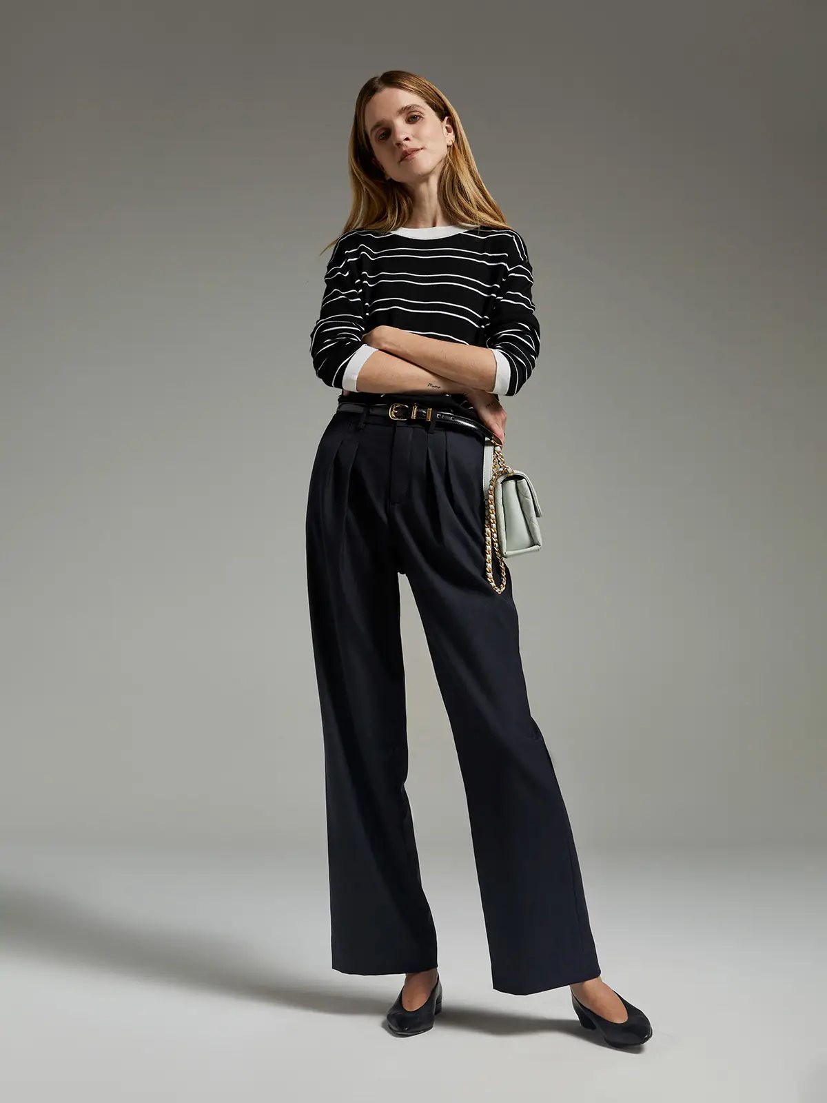 Model wearing Midnight Blue classic wool wide-leg trousers with pleats, striped top, and belt, arms crossed.