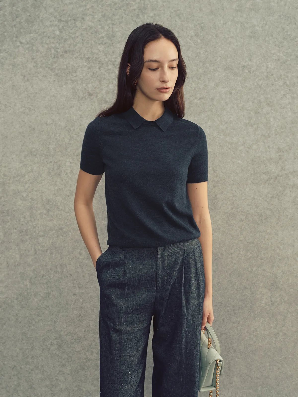 Model in charcoal AUDREY knit top with dark denim pleated trousers and mint quilted bag