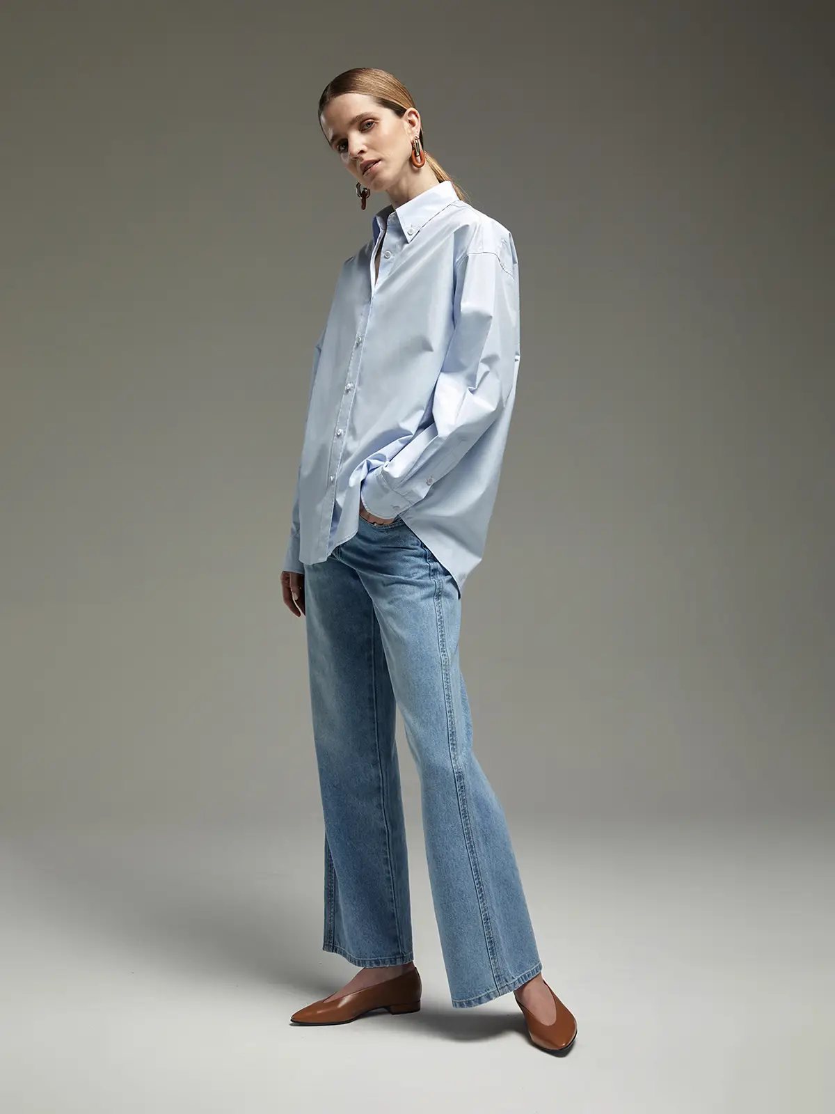 Model wearing a light blue oversized Pima cotton shirt with rolled sleeves, button-front closure, and relaxed fit.
