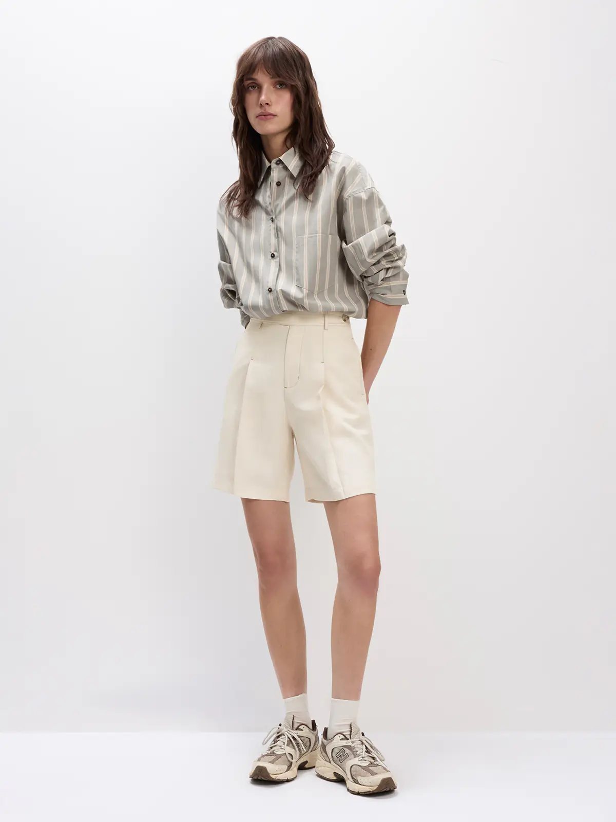 Model in a Grey striped oversized cotton shirt with rolled sleeves, paired with shorts and sneakers.