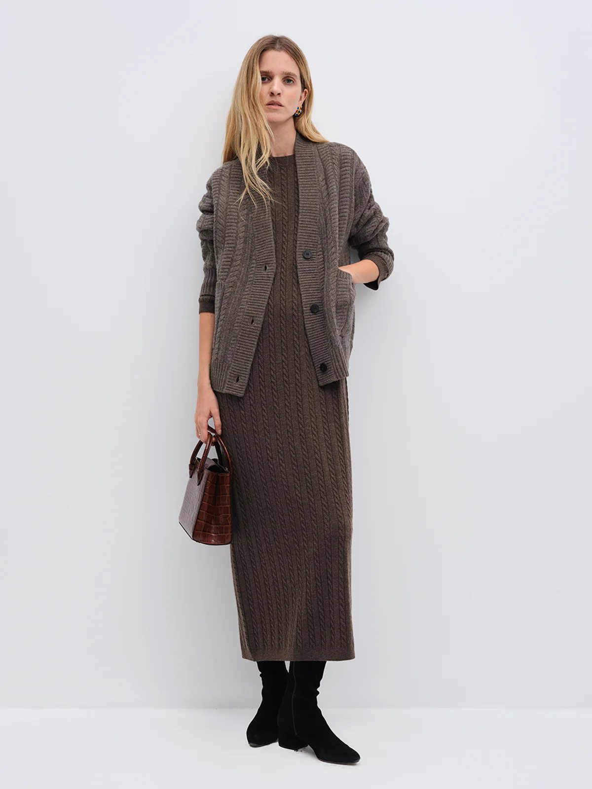 Model in andreatang dark brown Merino cable-knit maxi dress layered with tonal cardigan and black boots