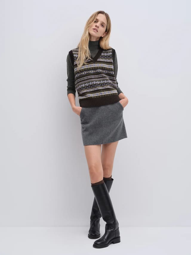 Model wearing a Brown Fair Isle knit vest with V-neck and ribbed hem over denim jeans.
