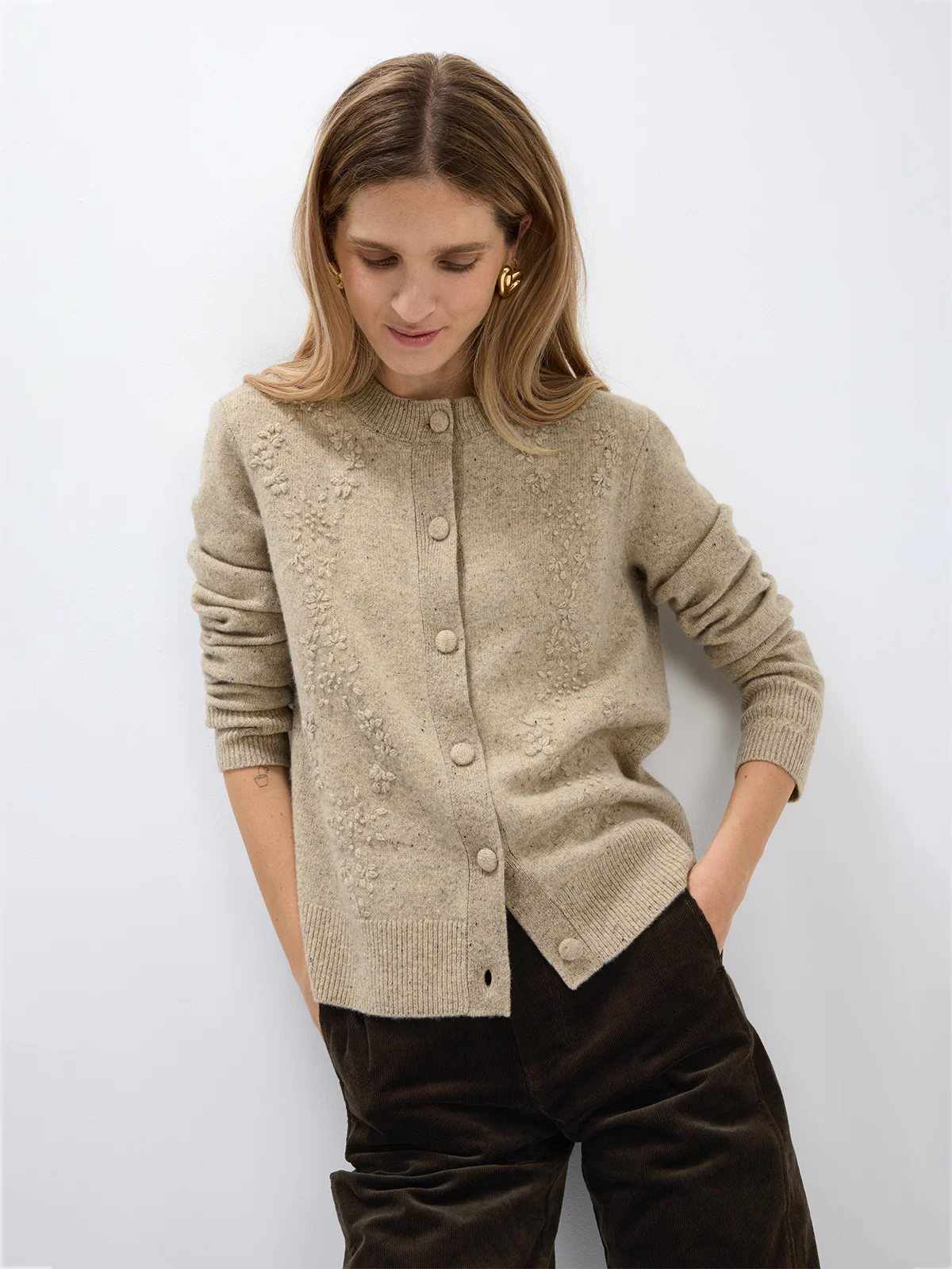Close-up of a model wearing a Light Brown Donegal knit cardigan showing floral texture, ribbed cuffs, and button closure.