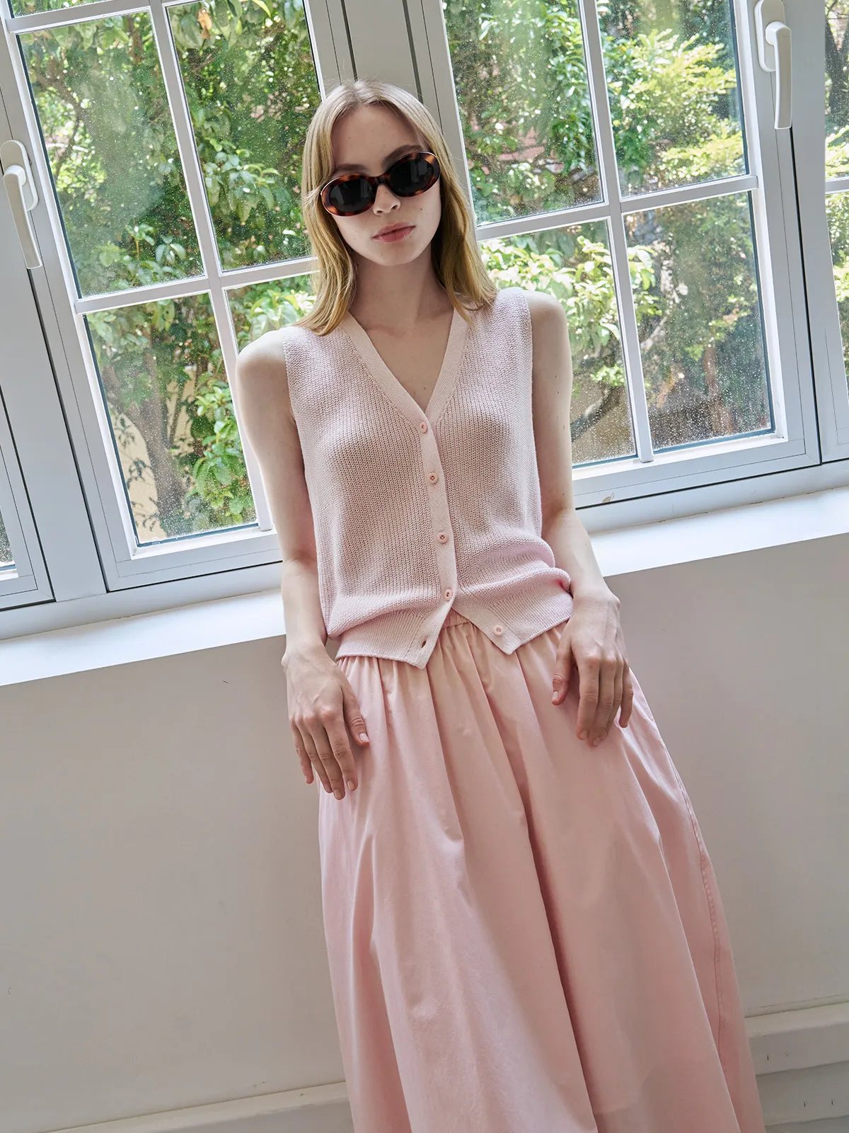 Model in blush pink ZOLA vest and matching midi skirt, standing by large window