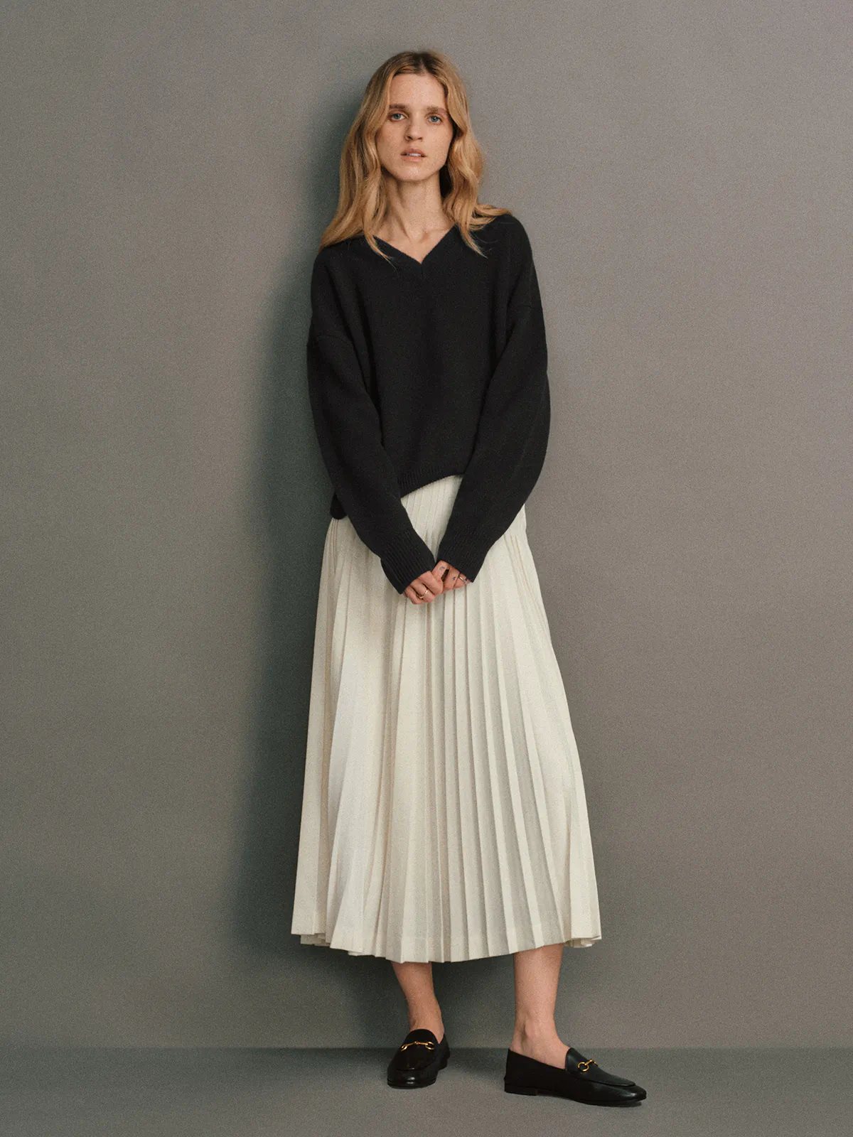 Front view of the Bottle Green CARRIE Merino Wool V-Neck Jumper styled with pleated trousers and pearl earrings.